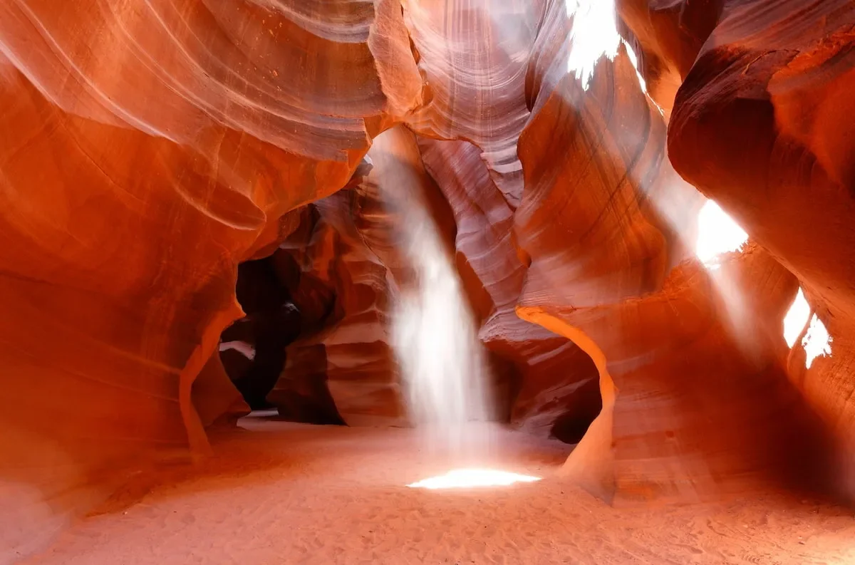 Inside Antelope Canyon with smooth, orange-red sandstone walls and a narrow beam of sunlight illuminating the canyon floor.