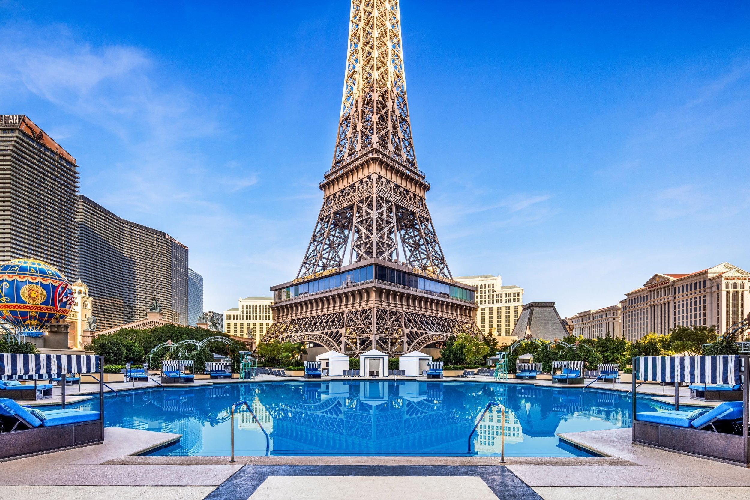 Las Vegas hotel pool area with the Eiffel Tower replica in the background and surrounding buildings under a clear blue sky.