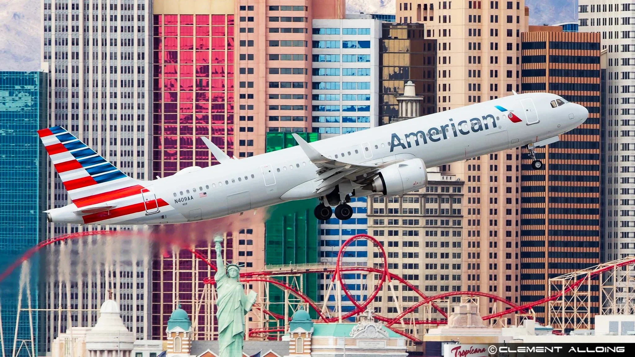 United States commercial airplane flying over Las Vegas with the city’s hotels, including replicas of the Statue of Liberty and a roller coaster in the background.