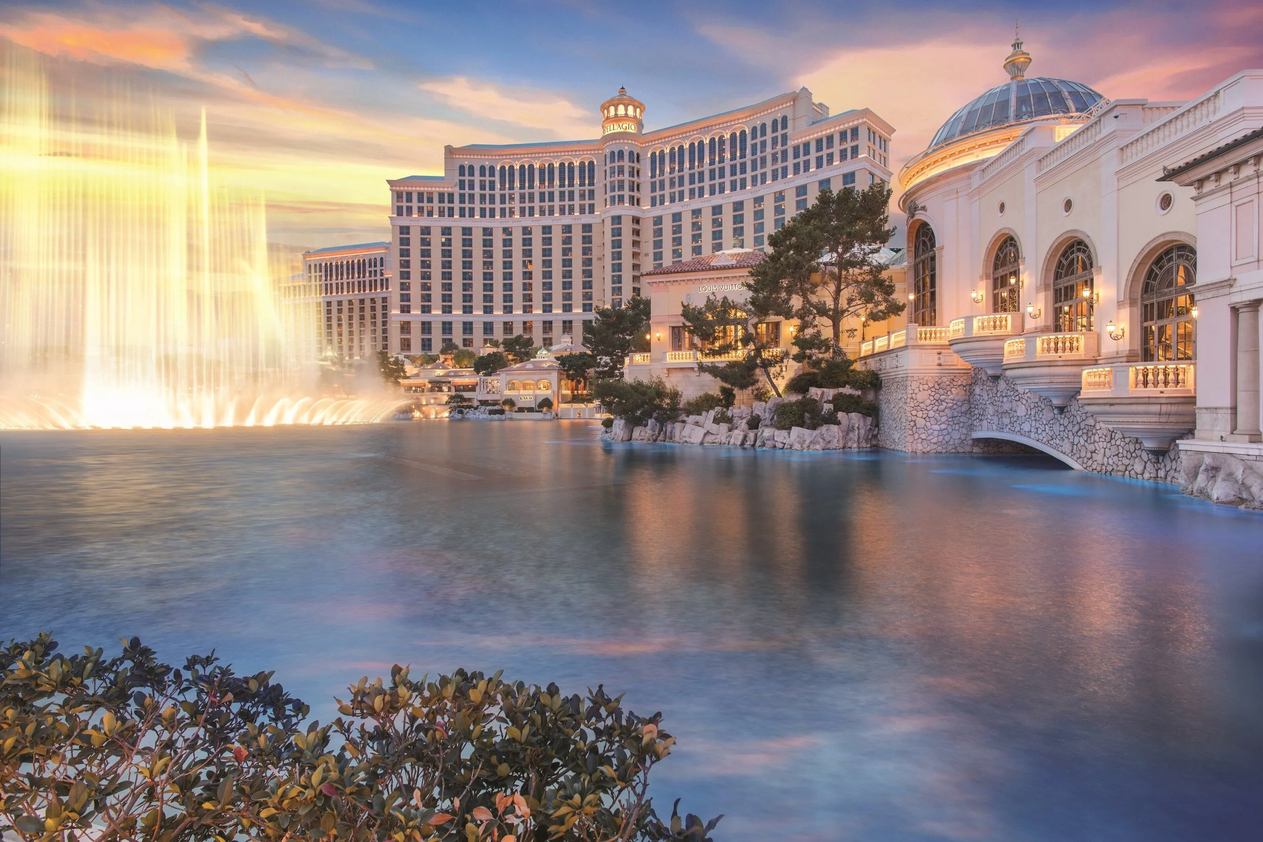 View of the Bellagio hotel and casino in Las Vegas with its fountains and a pastel-colored sunset sky.