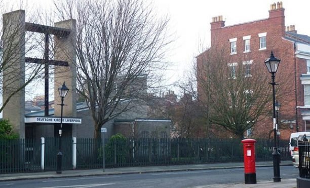 Street view with trees, street lamps, a red mailbox, and brick buildings in the background, in an urban area.