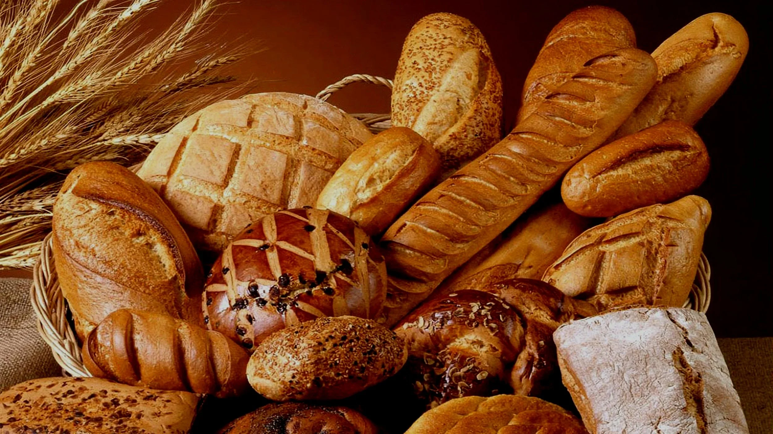 Assorted baked bread and rolls in a basket with wheat stalks.