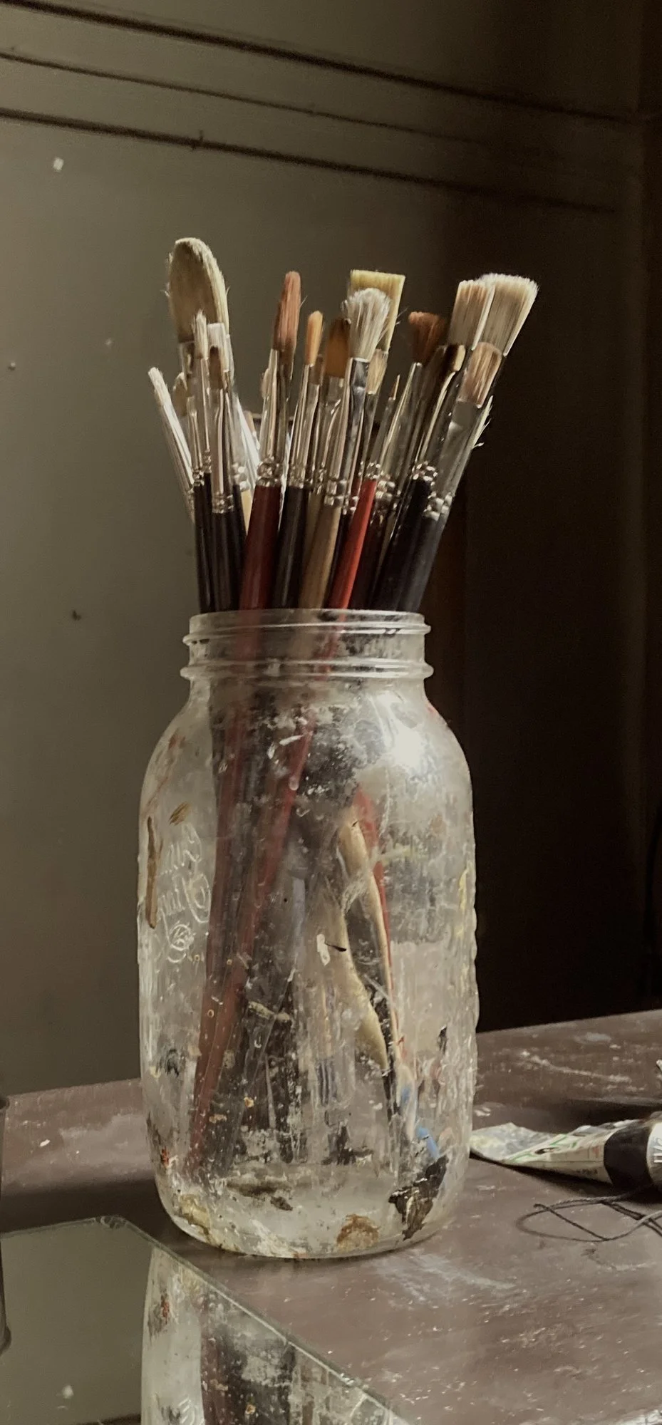 Glass jar of well-used paintbrushes with dried oil paint on the bristles, in Simon Broom's art studio