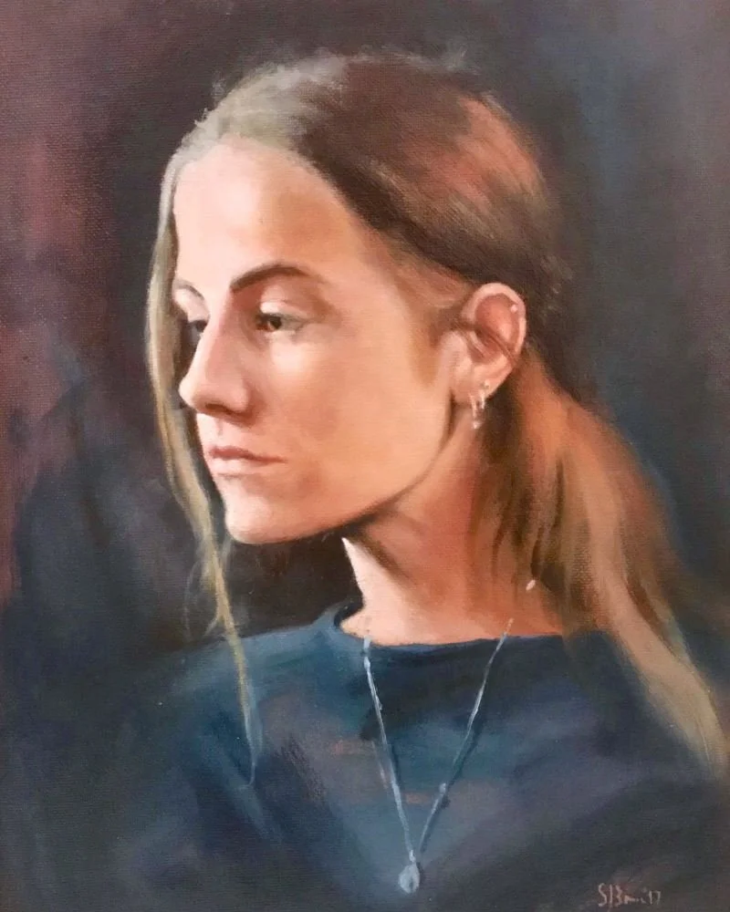 A portrait of a young woman with long brown hair, wearing earrings and a necklace, looking to the side with a contemplative expression.  Simon Broom