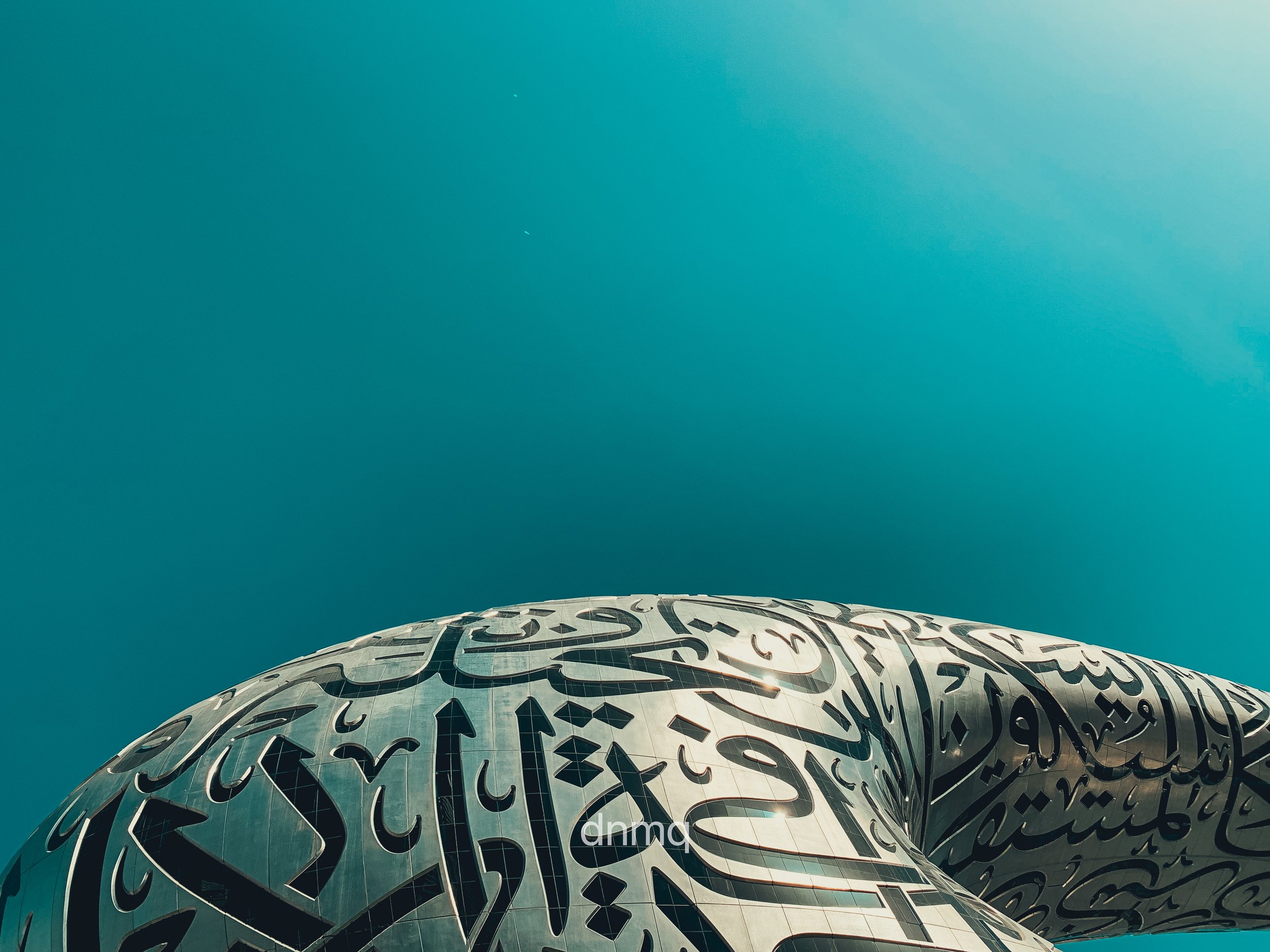 Close-up of the underside of a modern architectural building Museum of the future in Dubai with Arabic calligraphy design, against a clear blue sky.