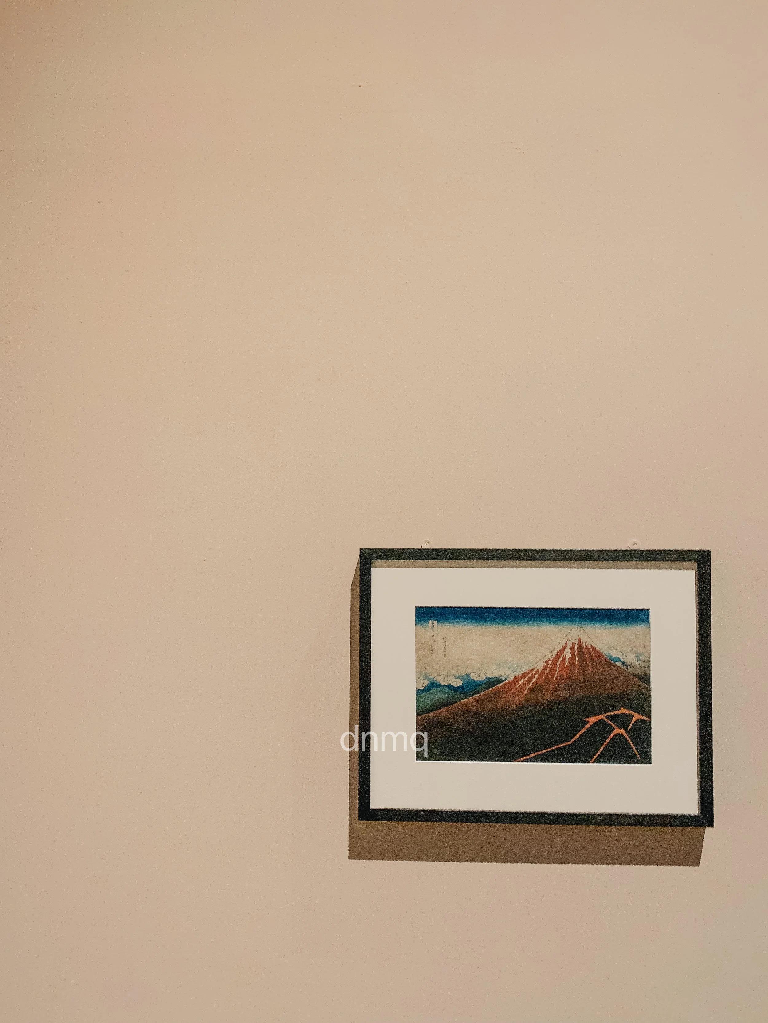 A framed picture of Mount Fuji with surrounding mountains on a beige wall.