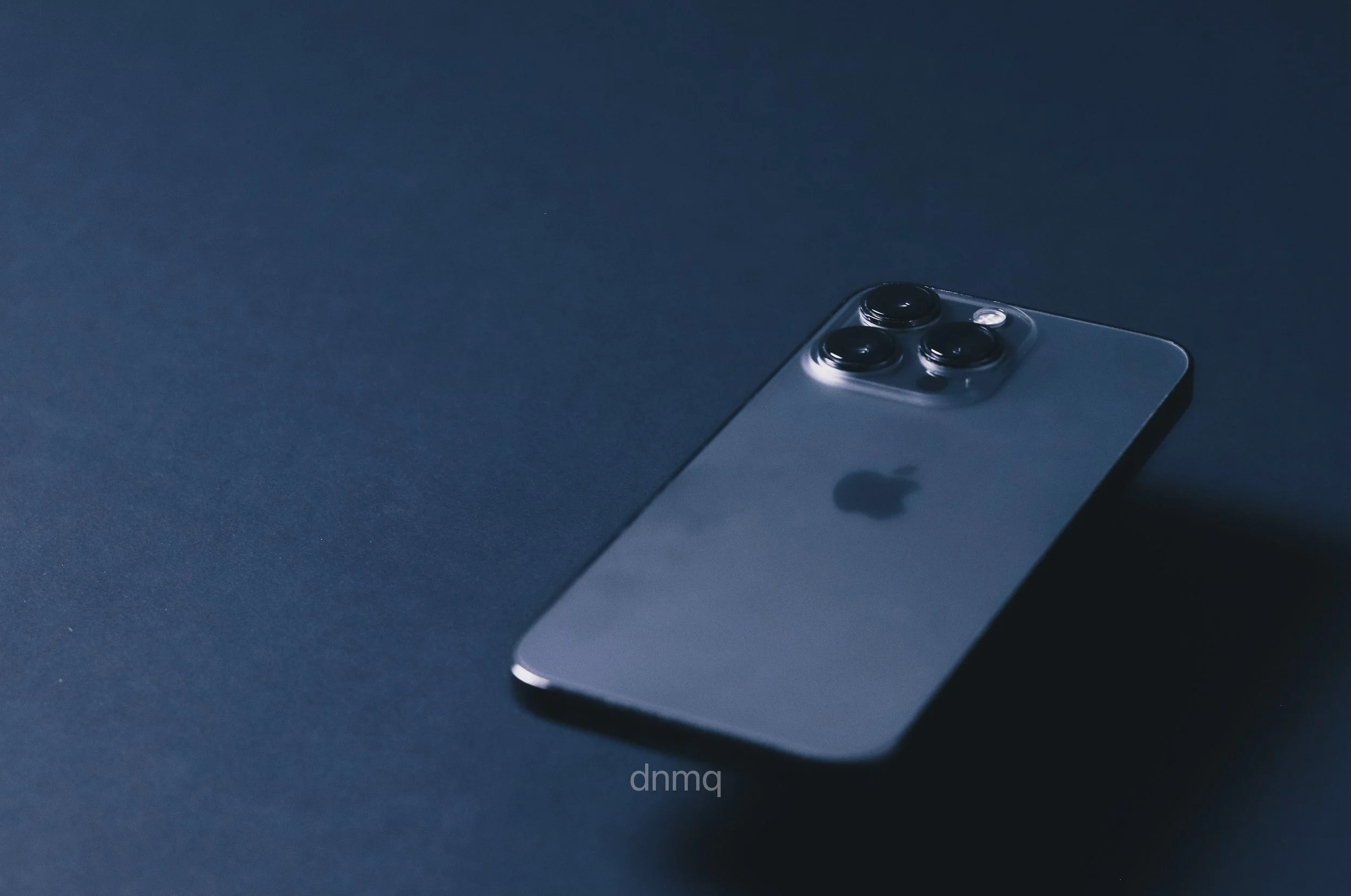 An iPhone with a triple-camera system on its back, lying on a dark surface.