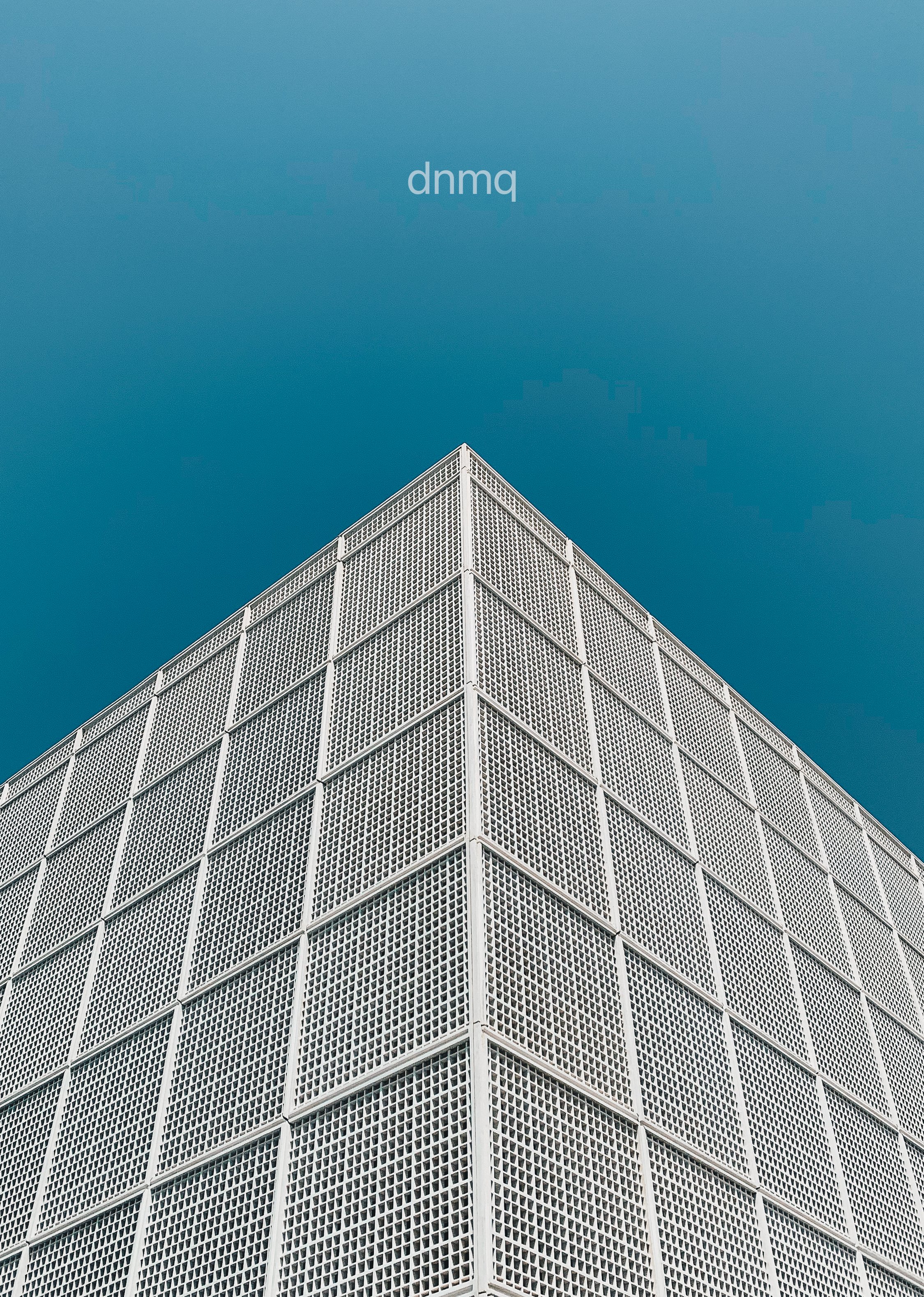 A white building with a grid pattern of square openings, viewed from below against a clear blue sky.