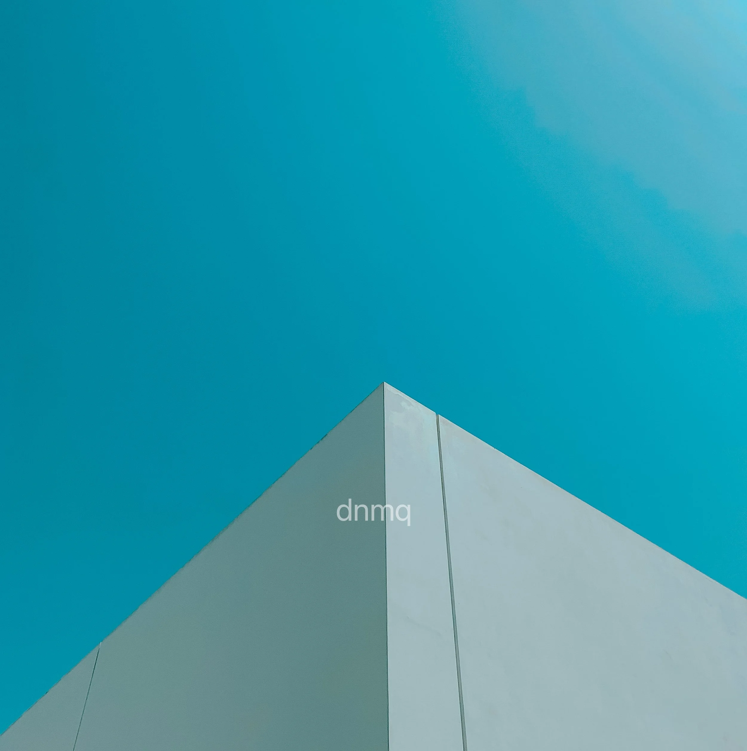 A minimalist photograph of a modern building corner with a plain white facade against a clear bright blue sky.