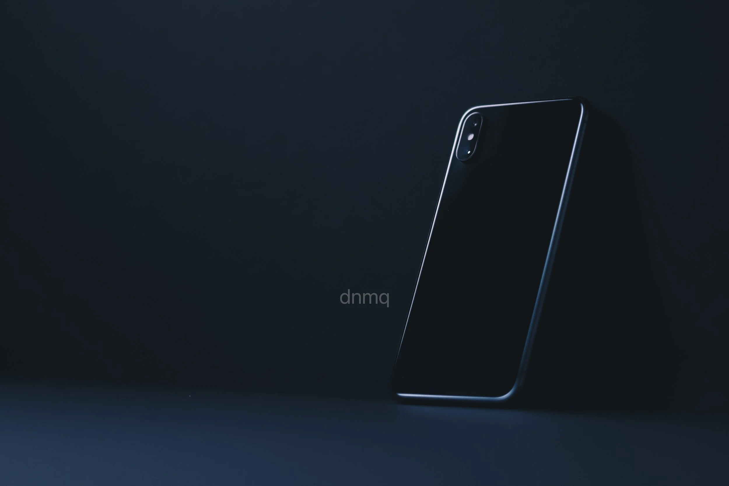 A black smartphone standing upright on a dark surface against a dark background.