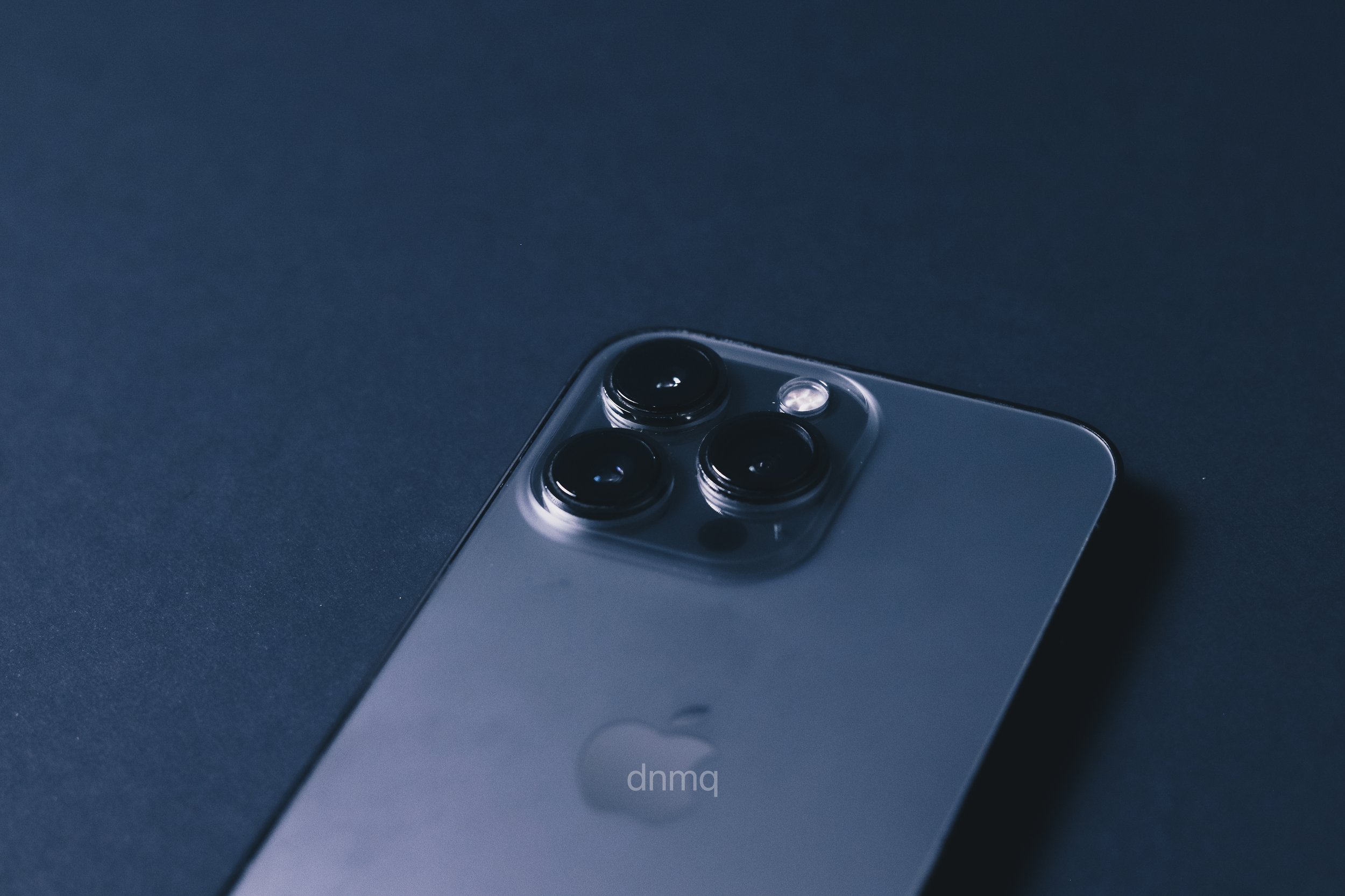 The back of a modern smartphone with a triple-lens camera and flash, placed on a dark surface.