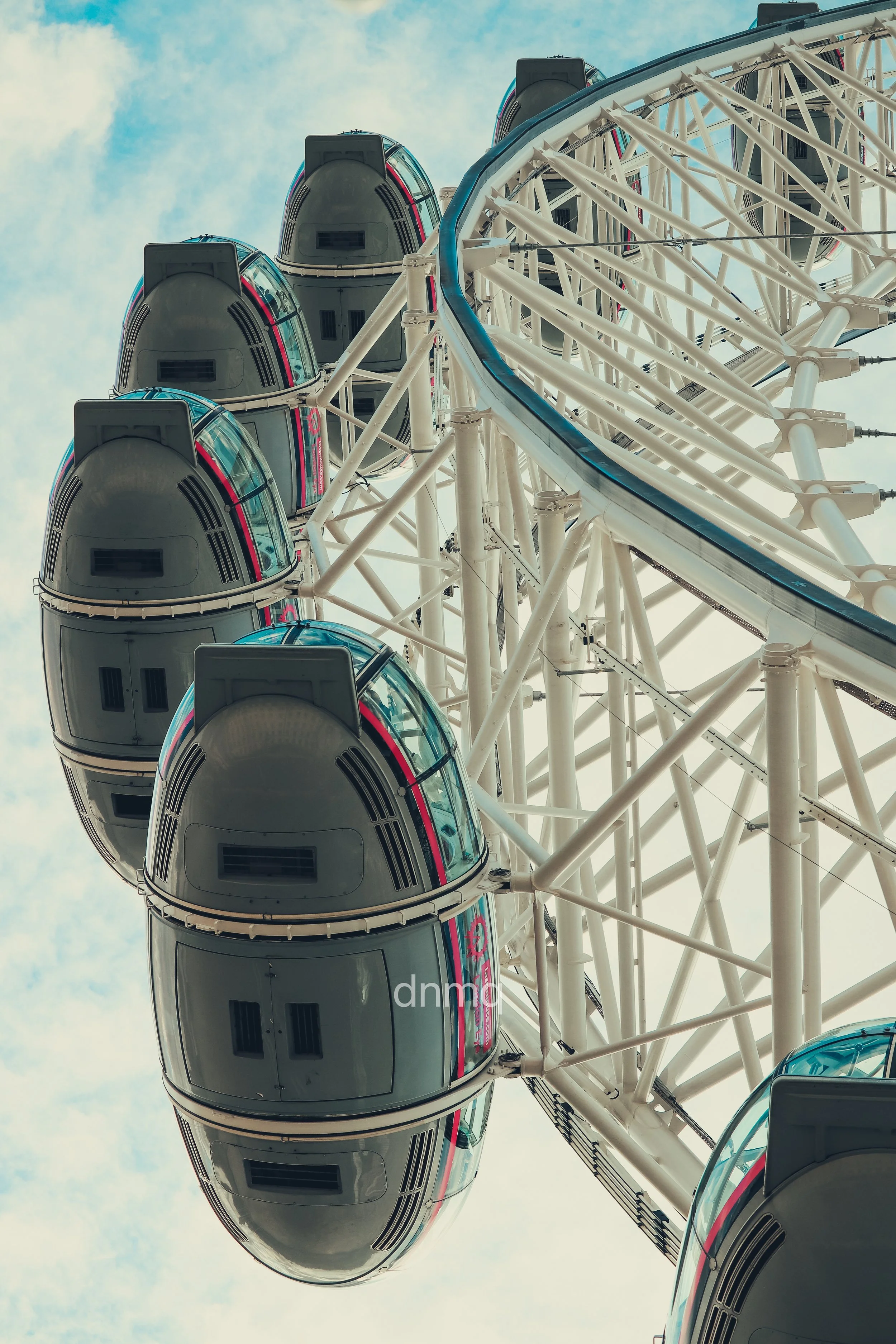 Close-up of a Ferris wheel with enclosed gondolas against a cloudy sky, viewed from below.