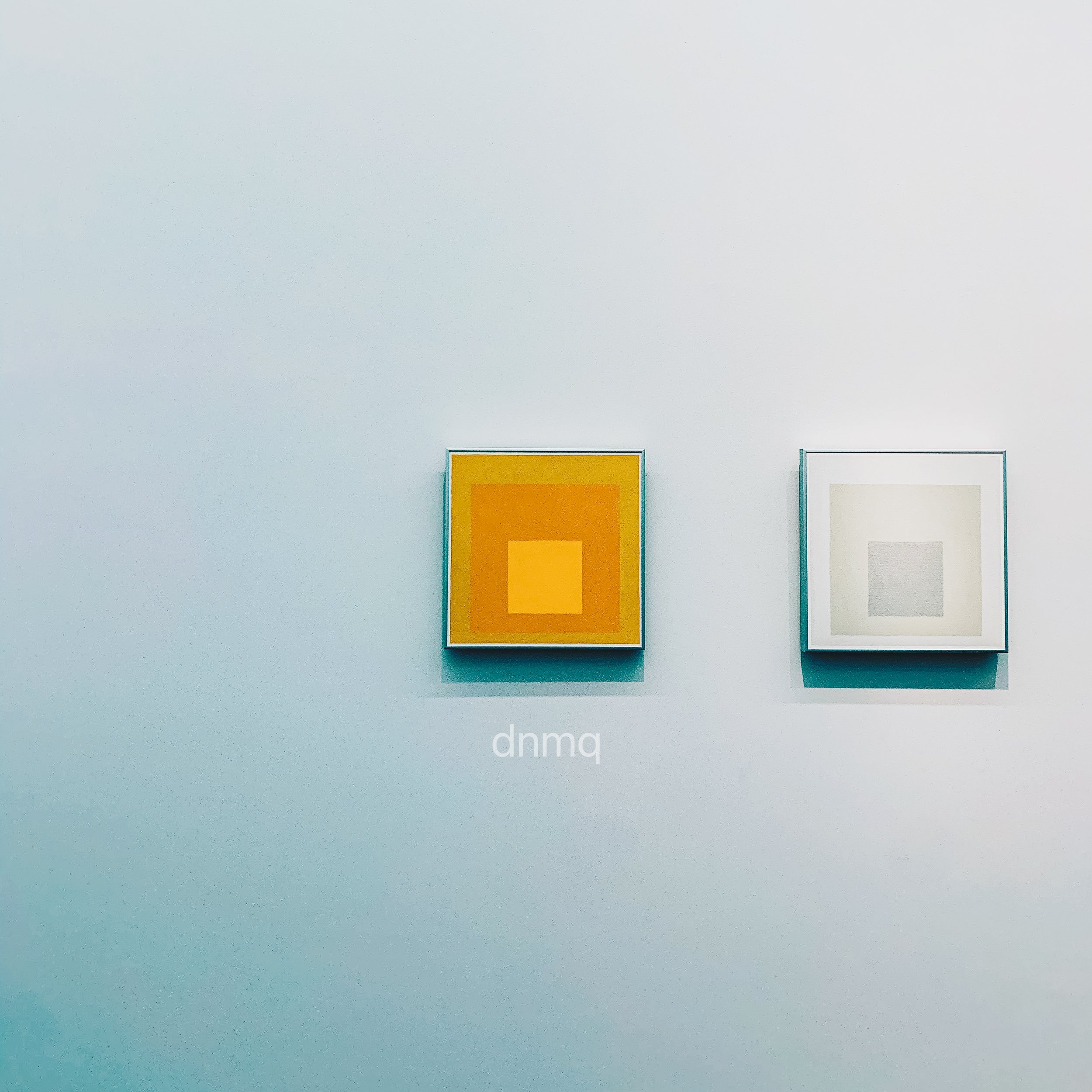 Two framed abstract artworks hanging on a white gallery wall. The artwork on the left features concentric squares in shades of yellow and orange, and the one on the right features concentric squares in shades of gray and beige.