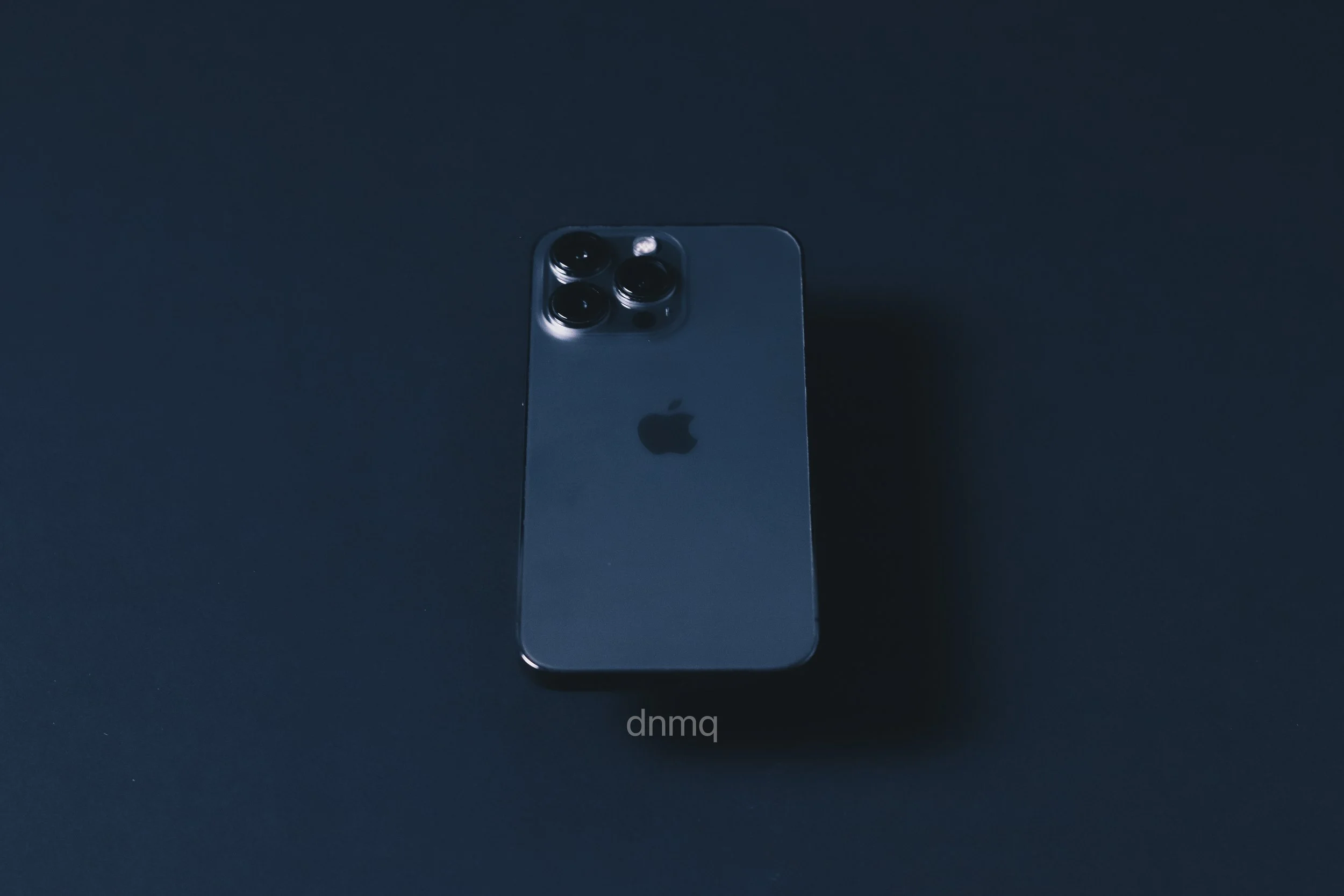 A dark-colored iPhone with triple camera lenses on the back, placed on a dark surface.