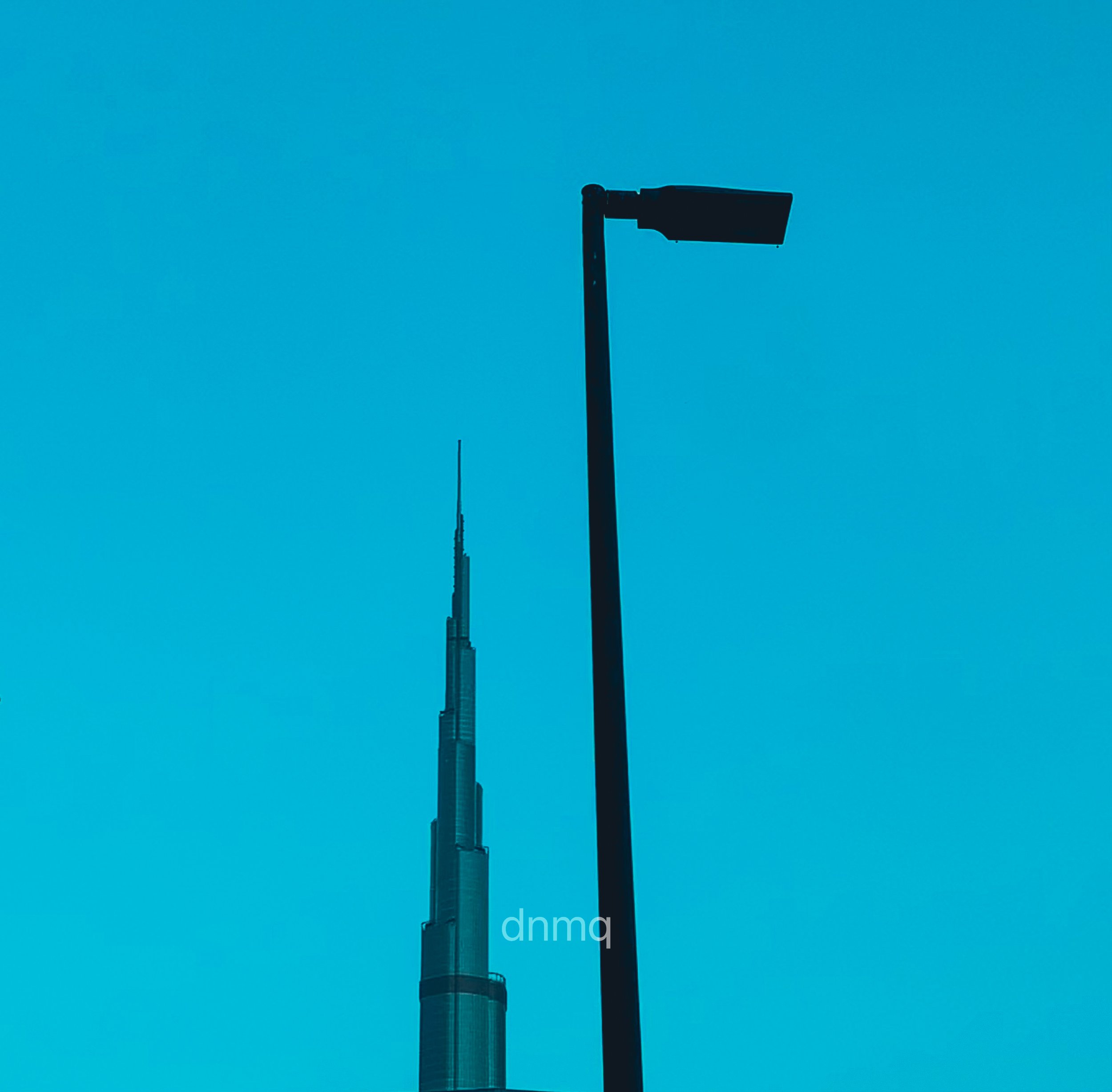 Silhouettes of a streetlight and the Burj Khalifa against a clear blue sky.