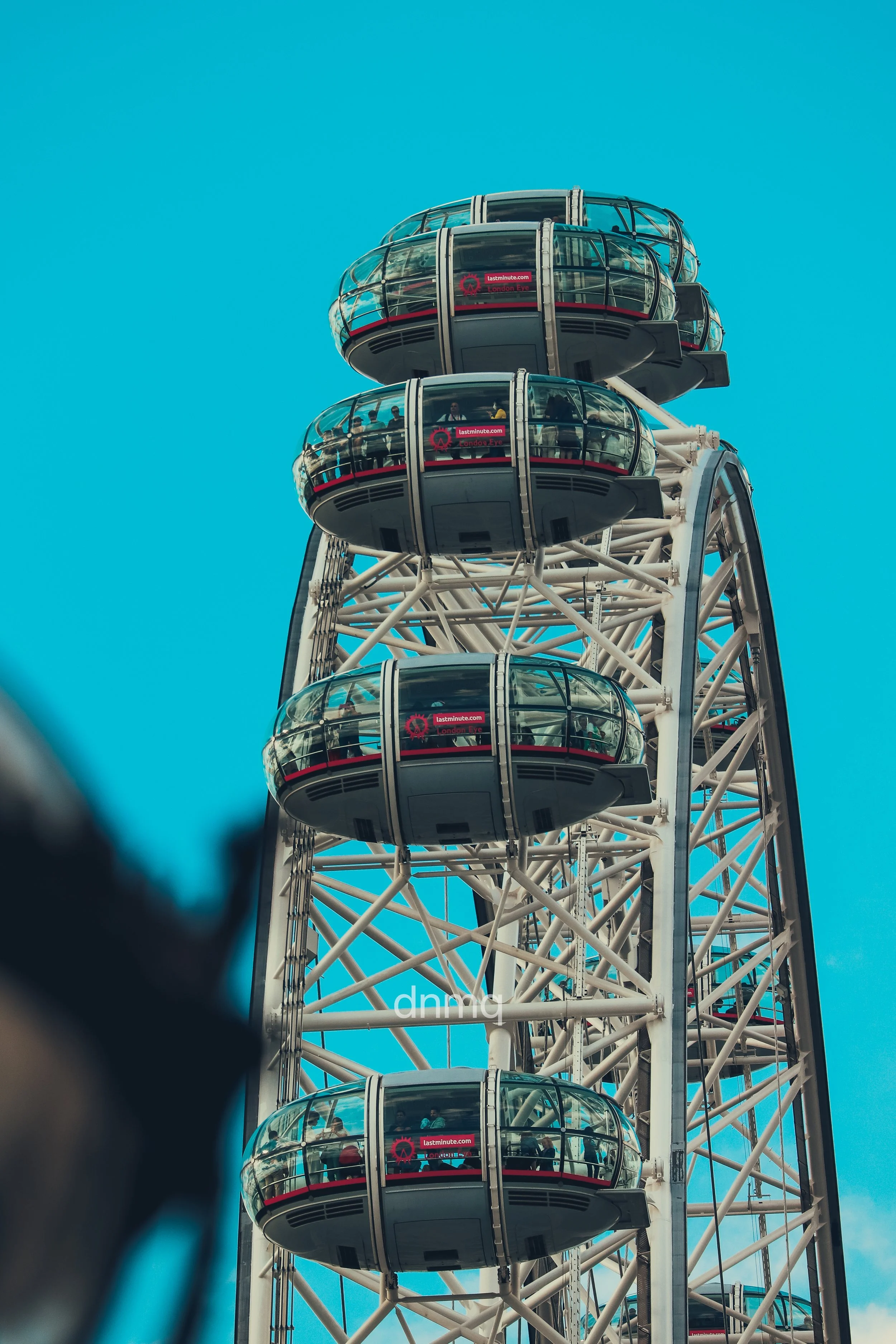 Close-up of the London Eye with enclosed passenger capsules against a bright blue sky.