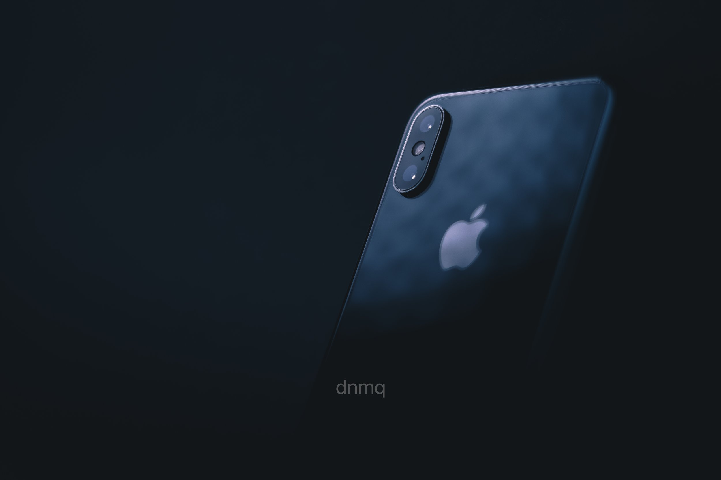A black iPhone with a three-camera system on the back, illuminated by soft lighting, set against a dark background.
