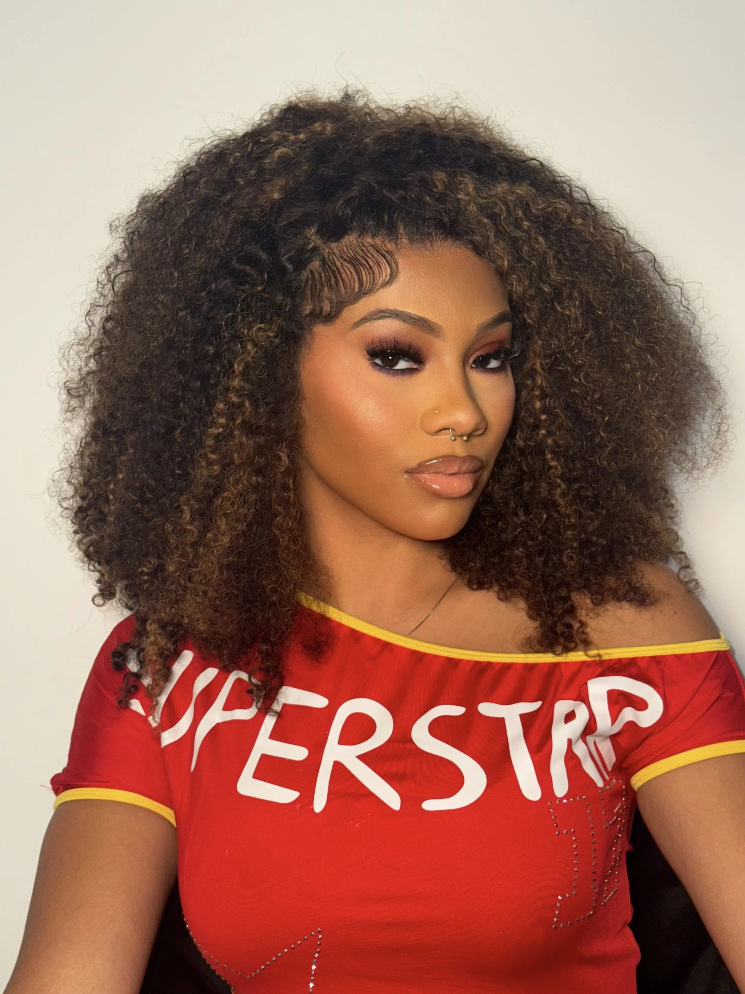 A woman with curly hair wearing a red upper with the word 'OVERSTRE' on it, posing against a plain white background.