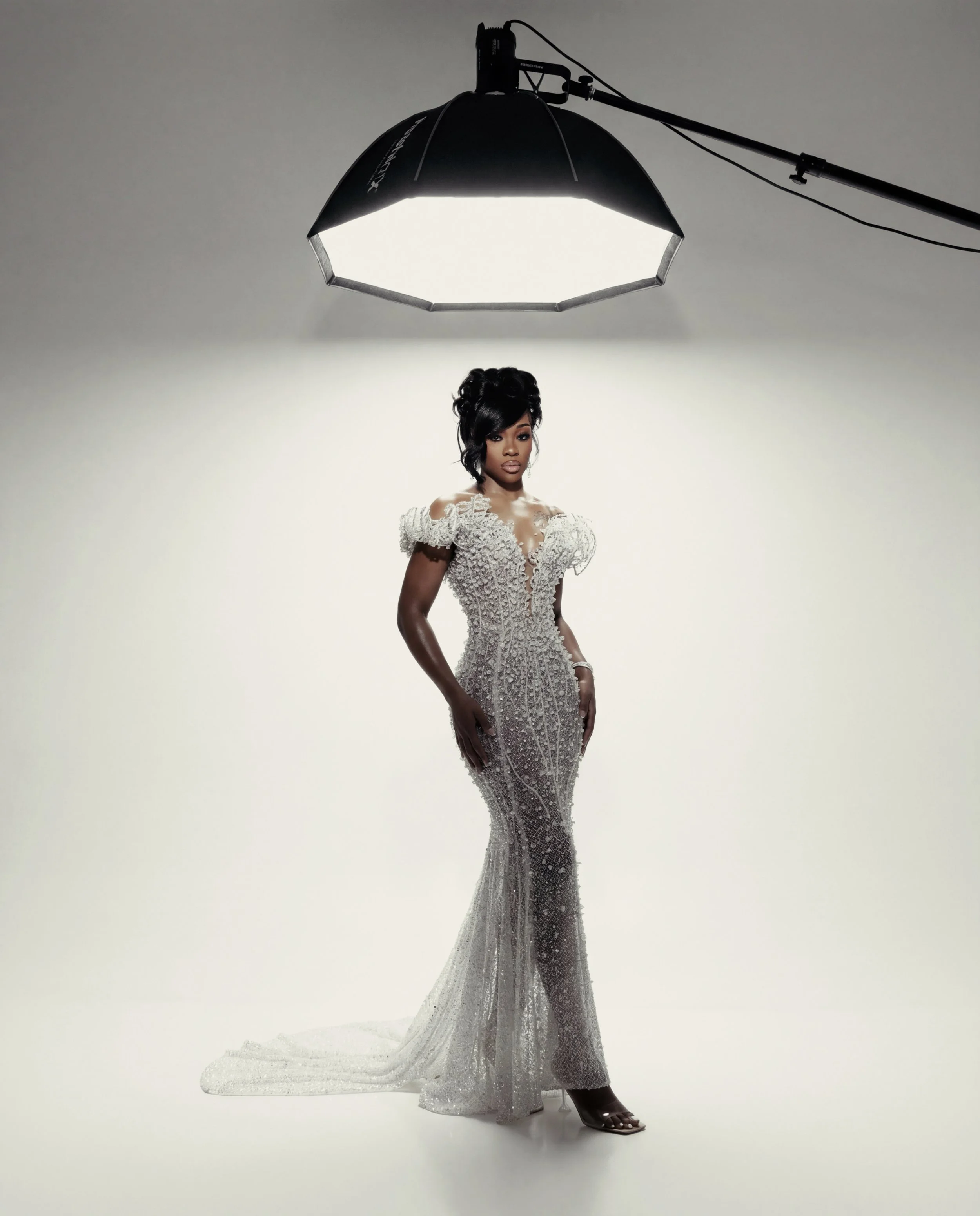 A woman in a fitting, sparkly, white gown under professional studio lighting.