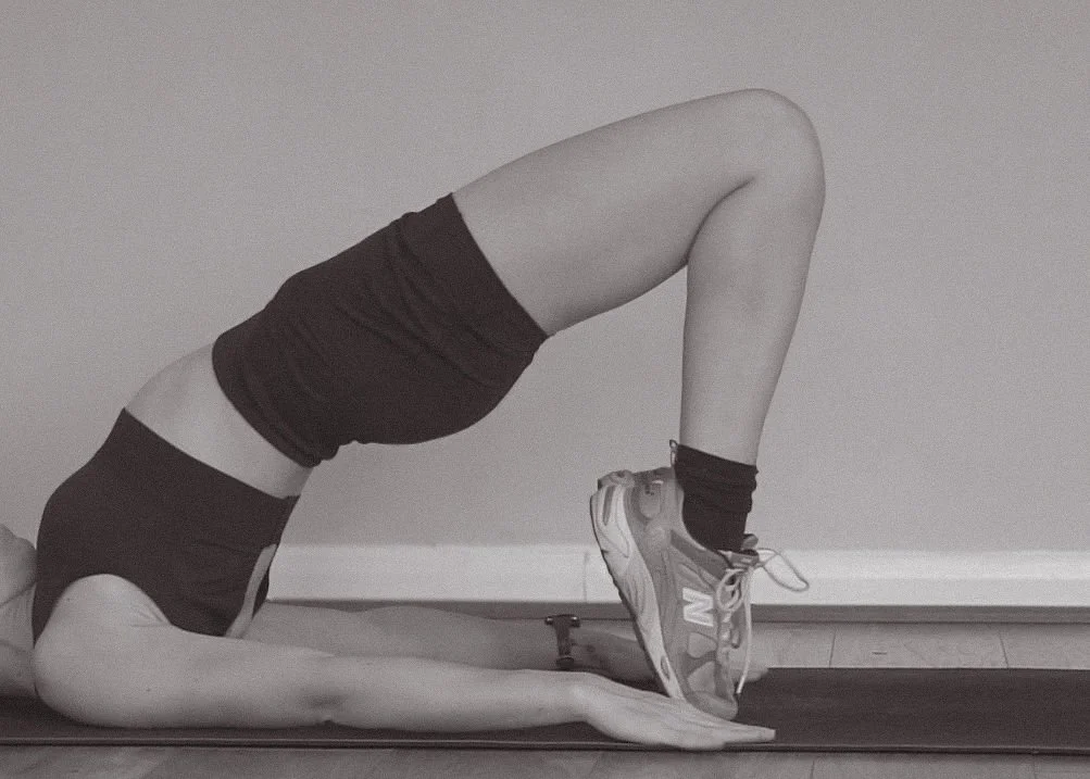 Person lying on their back on a yoga mat, performing a bridge exercise with legs bent, feet flat on the floor, and hips lifted.