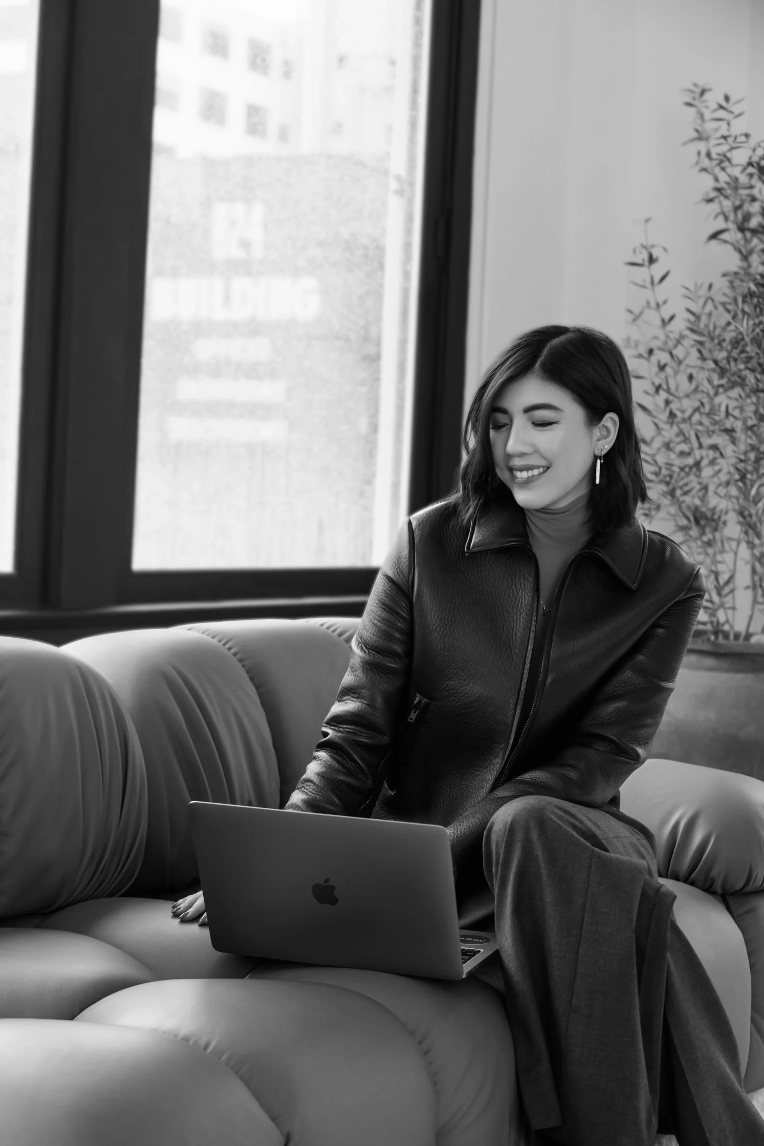 Women sitting on a sofa with a laptop in a bright room, smiling. Black and white photo.