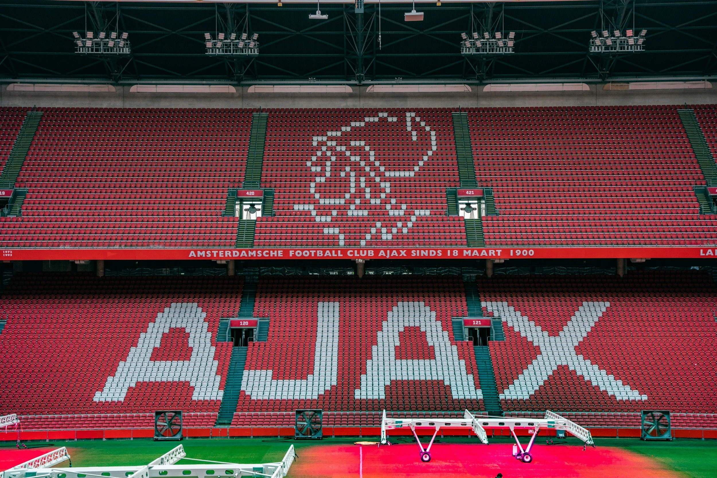 Empty football stadium with red seats spelling out 'AJAX' and an Ajax logo made of white seats on the upper level.