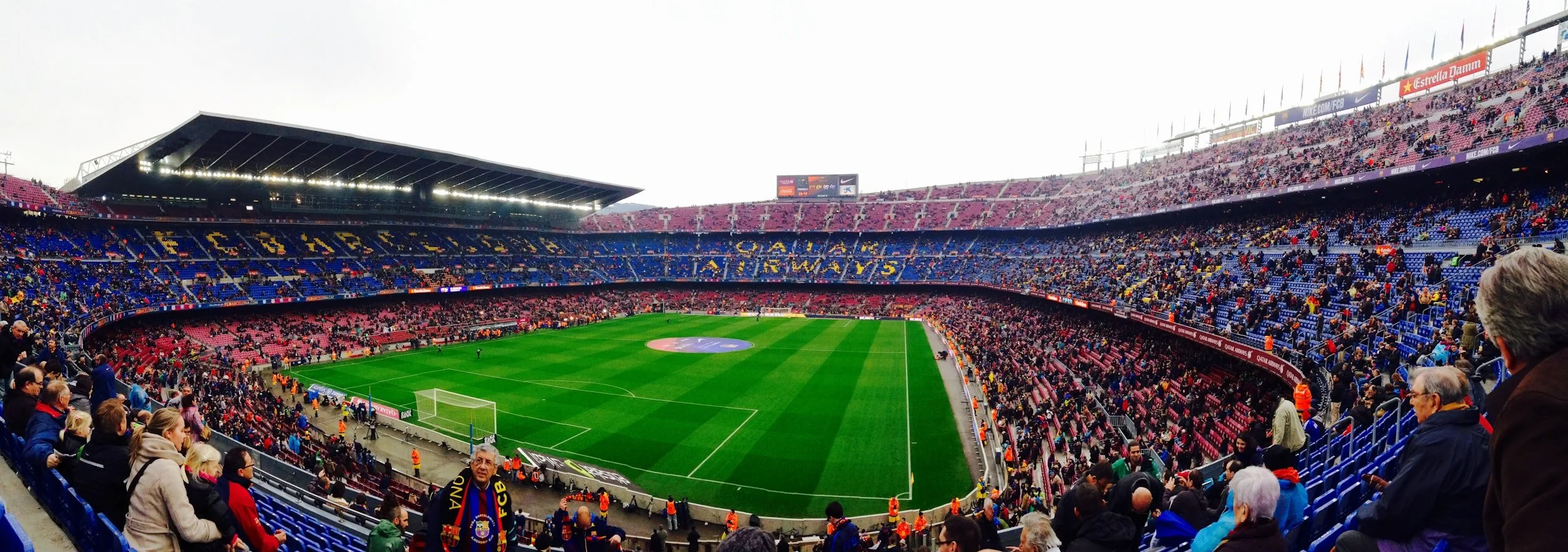 View of a packed soccer stadium with fans, a green field, and seating sections in blue and red, during a match.