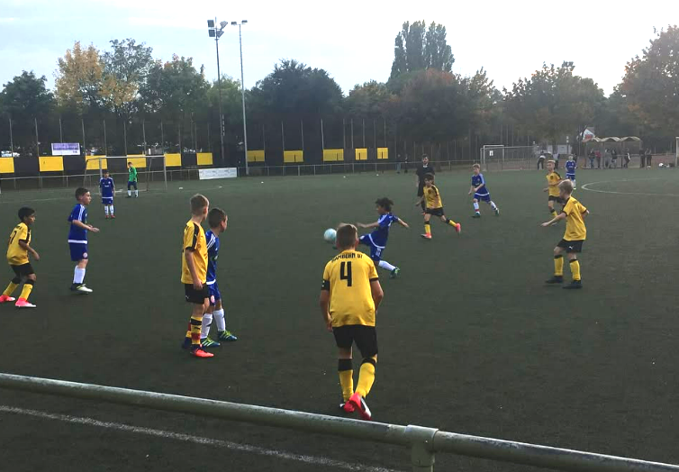 Children playing soccer on an outdoor field, with some in yellow jerseys and others in blue jerseys, during daytime.
