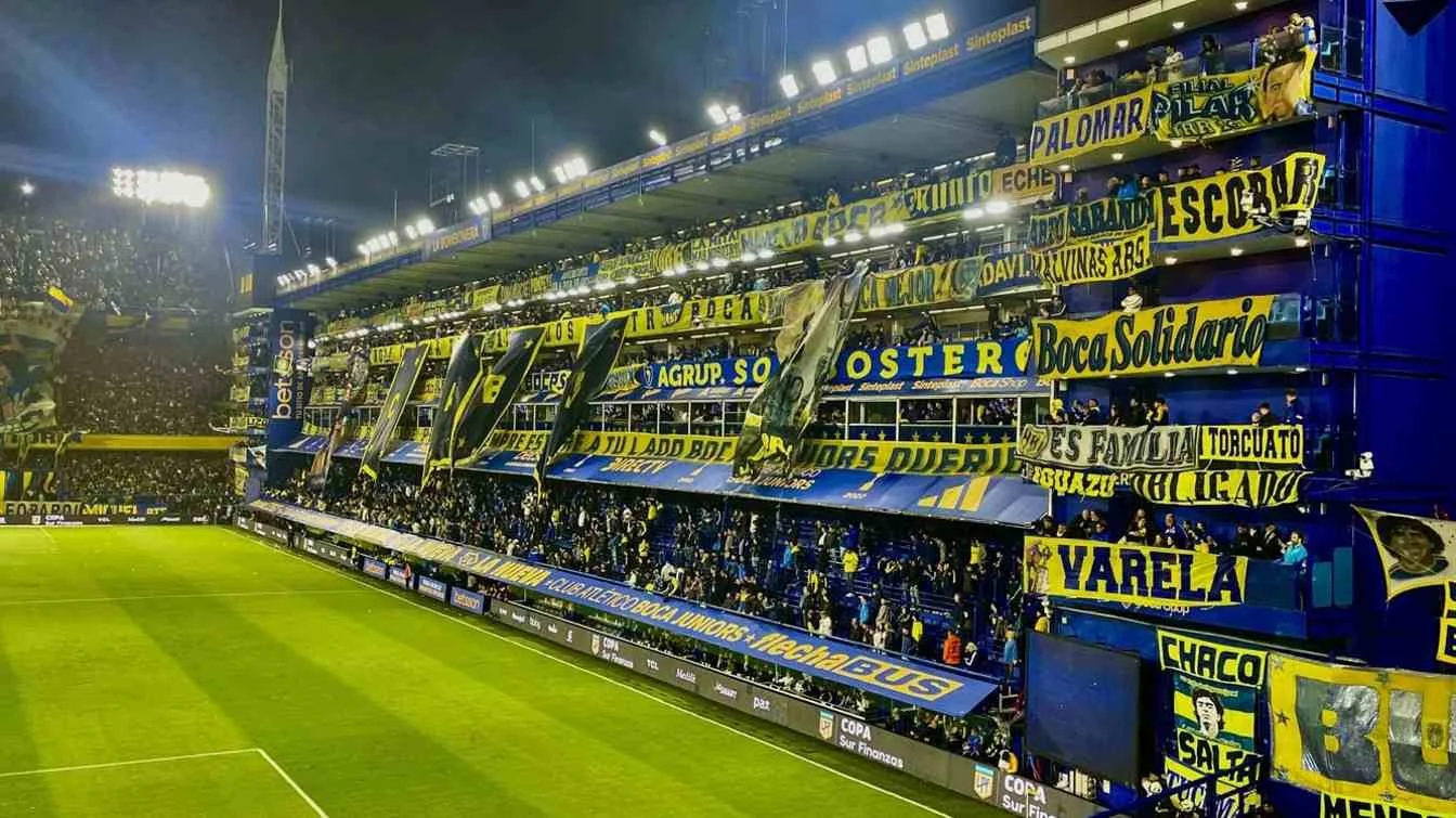 A crowded soccer stadium filled with fans holding yellow and blue banners and flags.