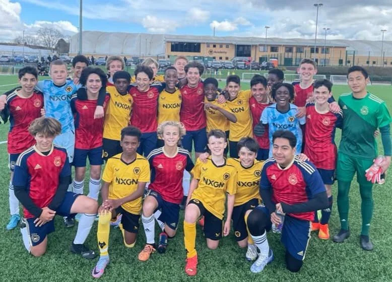 A group of young boys and a coach on a soccer field, wearing soccer uniforms of two different teams in red and yellow, posing for a team photo.
