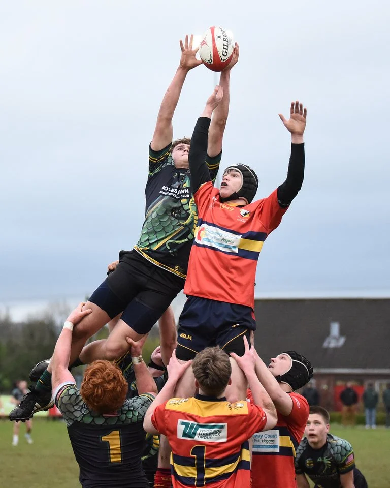 Rugby players engaging in a line-out, with players lifting a jumper to catch the ball during a match on a grassy field.