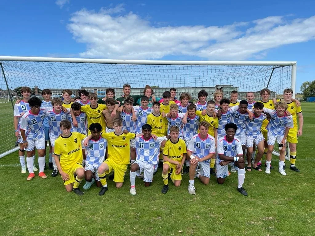 A youth soccer team posing for a team photo in front of a goal on a football field, with players in yellow and blue uniforms.