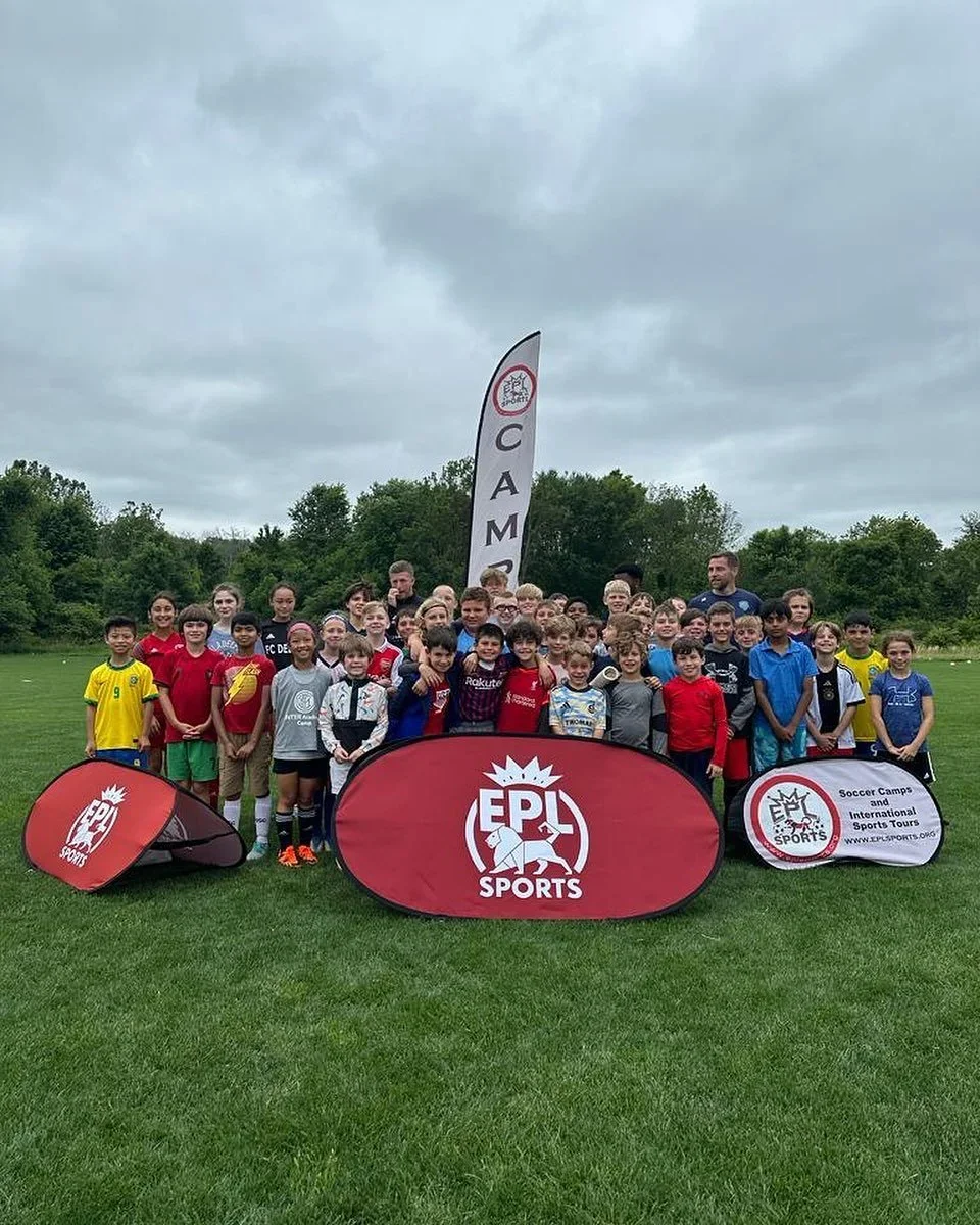 Group of children and coaches on a soccer field holding banners with the text 'EPL Sports' and 'Soccer Camps and International Sports Tours' during daytime with cloudy skies.