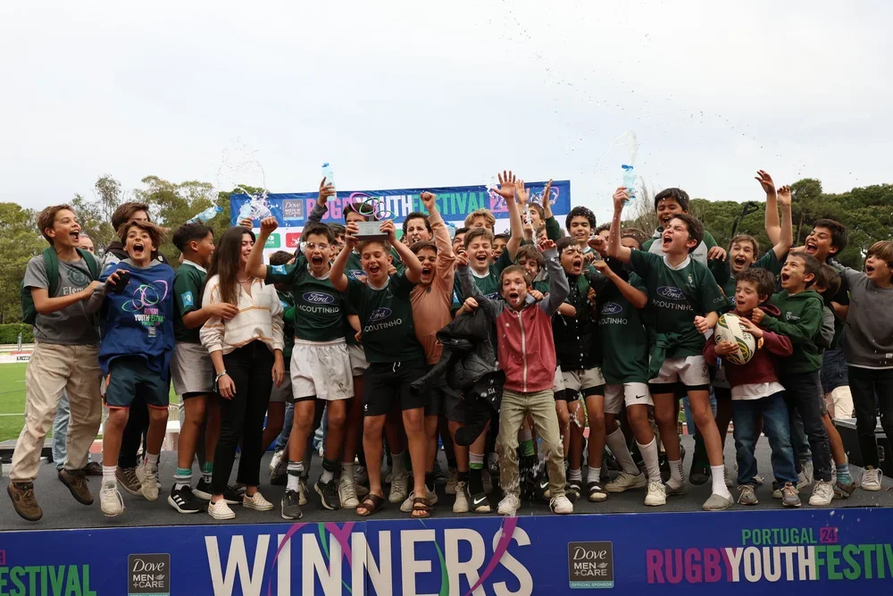Youth rugby team celebrating on stage with trophies, crowd cheering, and a banner reading 'Winners' at the Portugal Youth Rugby Festival.