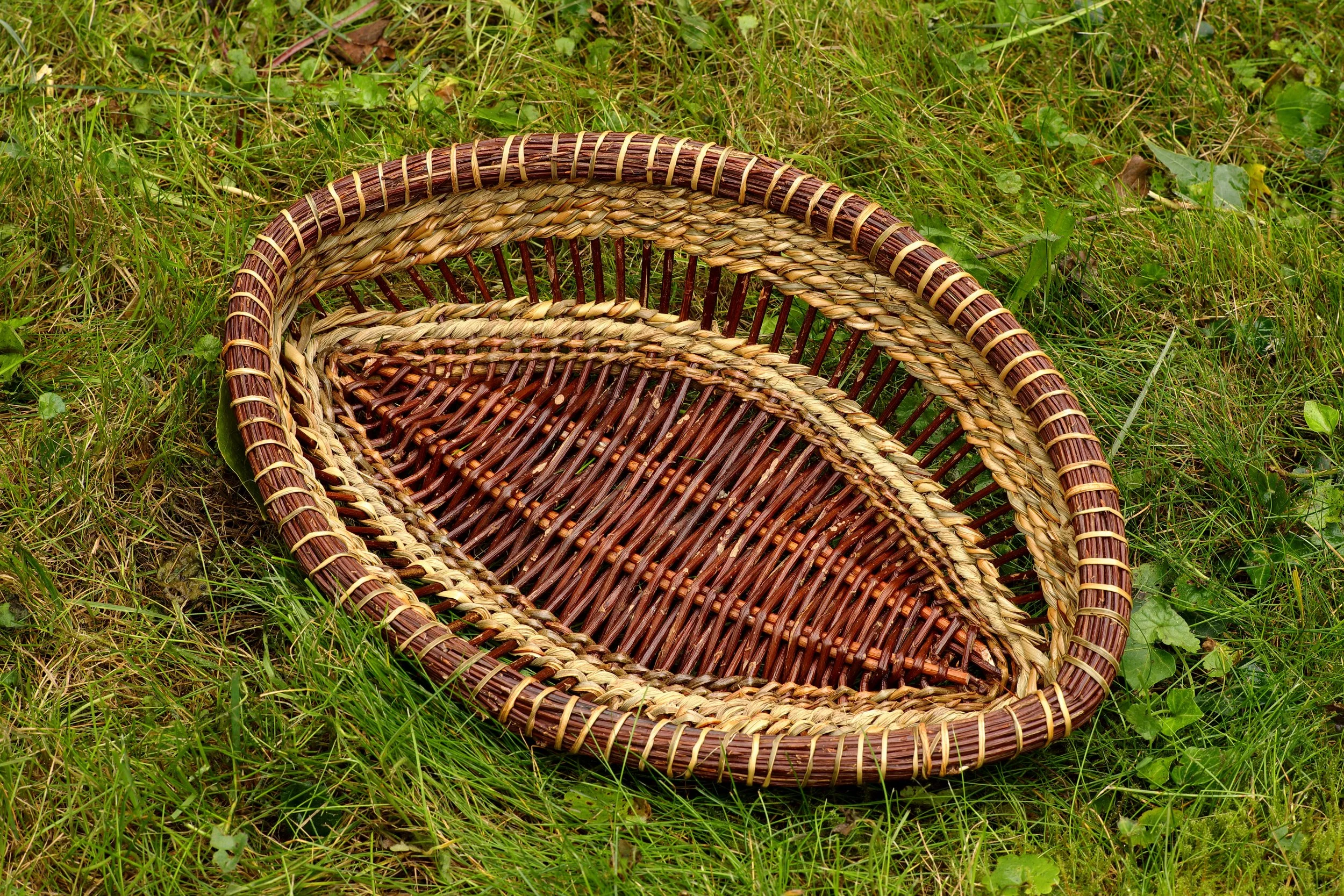 Cesta hecha de materiales naturales, colocada sobre césped verde.
