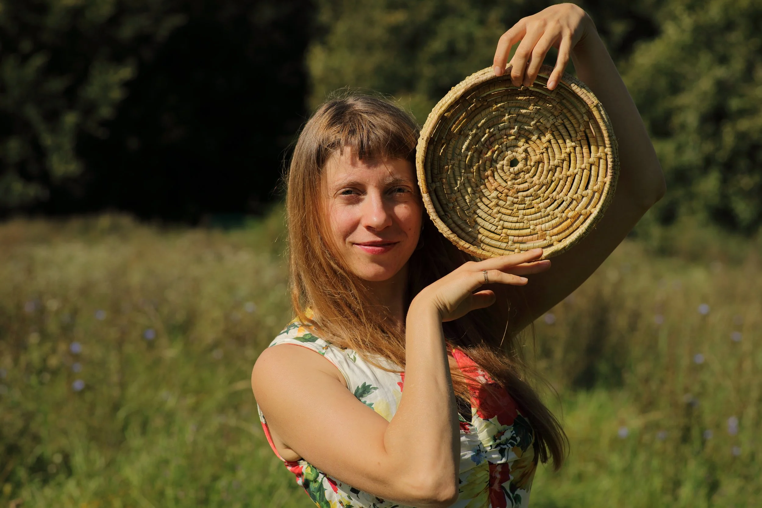 Mujer sonriente en un campo sosteniendo una cesta de phormium tenax.