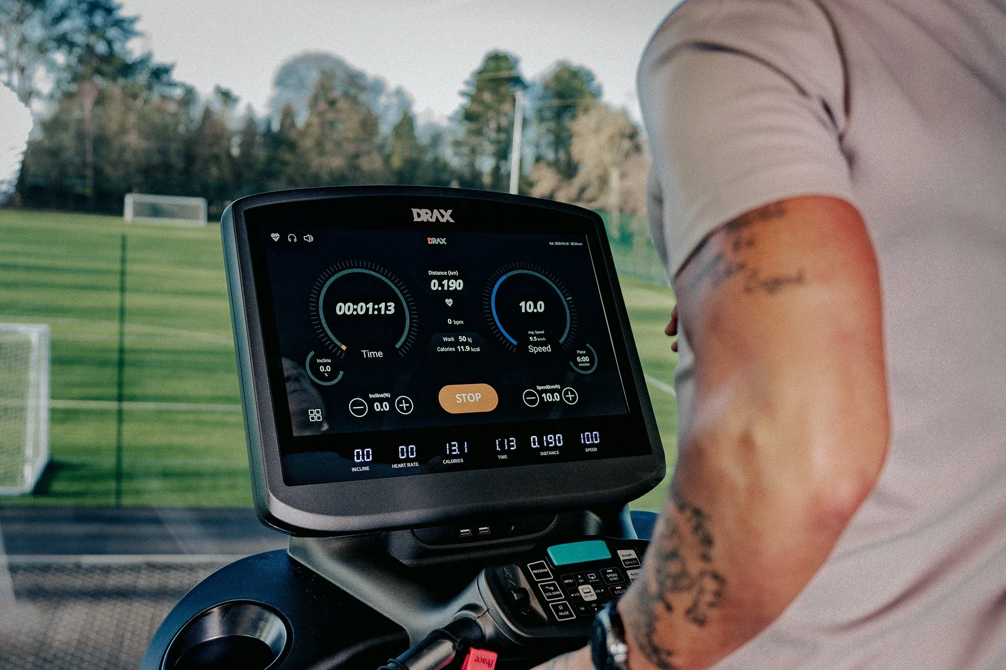 Close-up of a Drax cardio machine, with a person wearing a white shirt and tattoos on their arm.