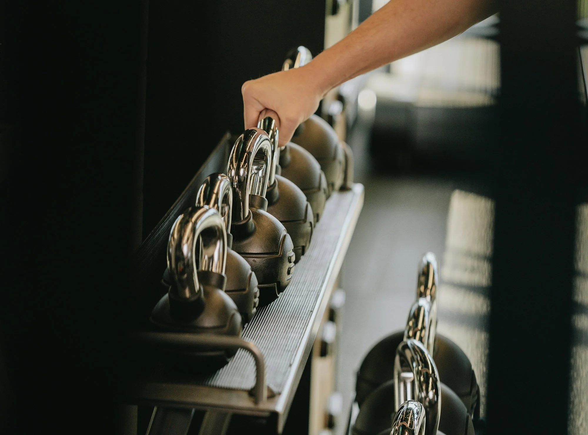 A person picking up a kettle bell from a rack.