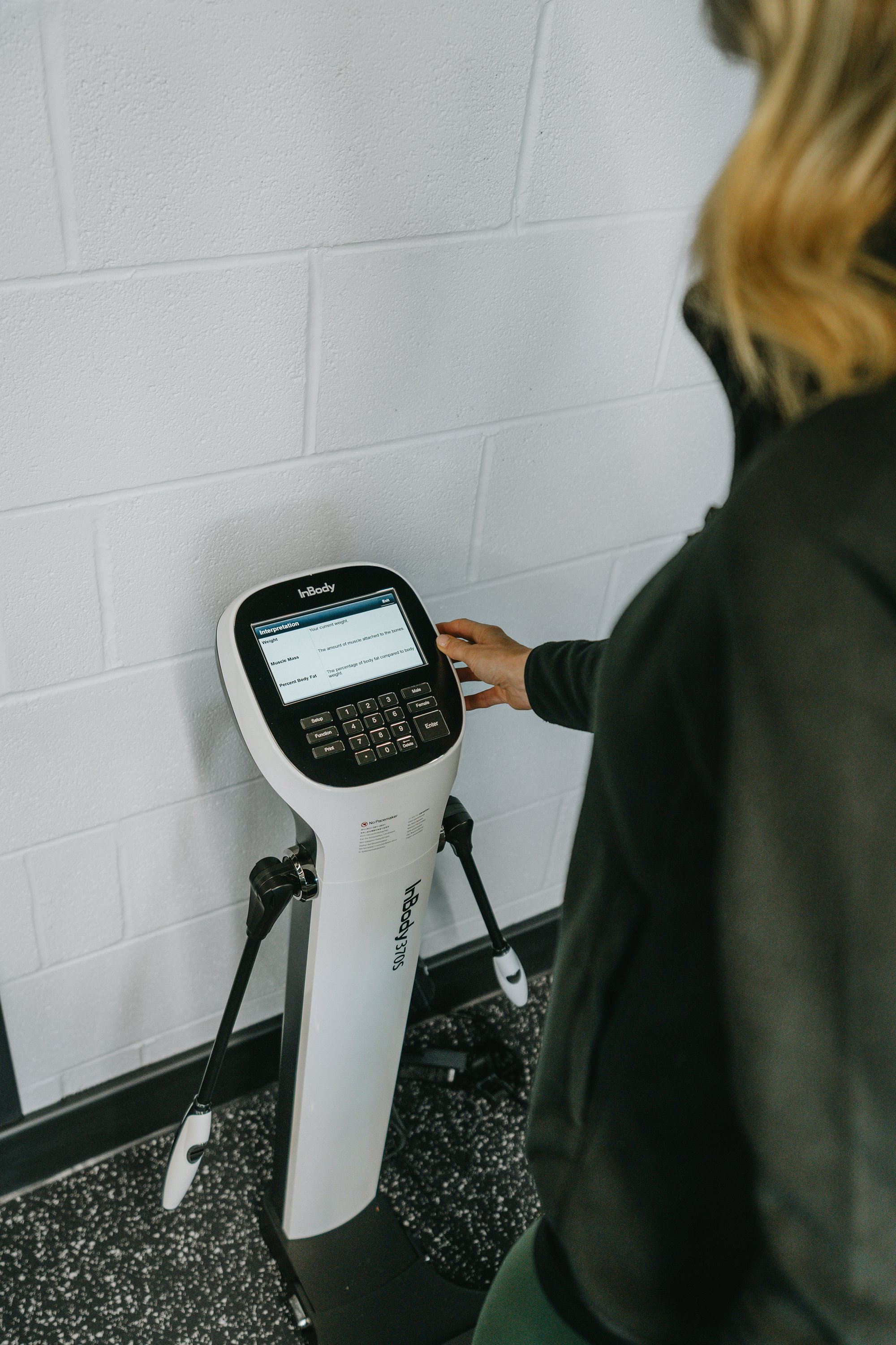 A person using an InBody body composition analyser machine in a room with white brick walls.