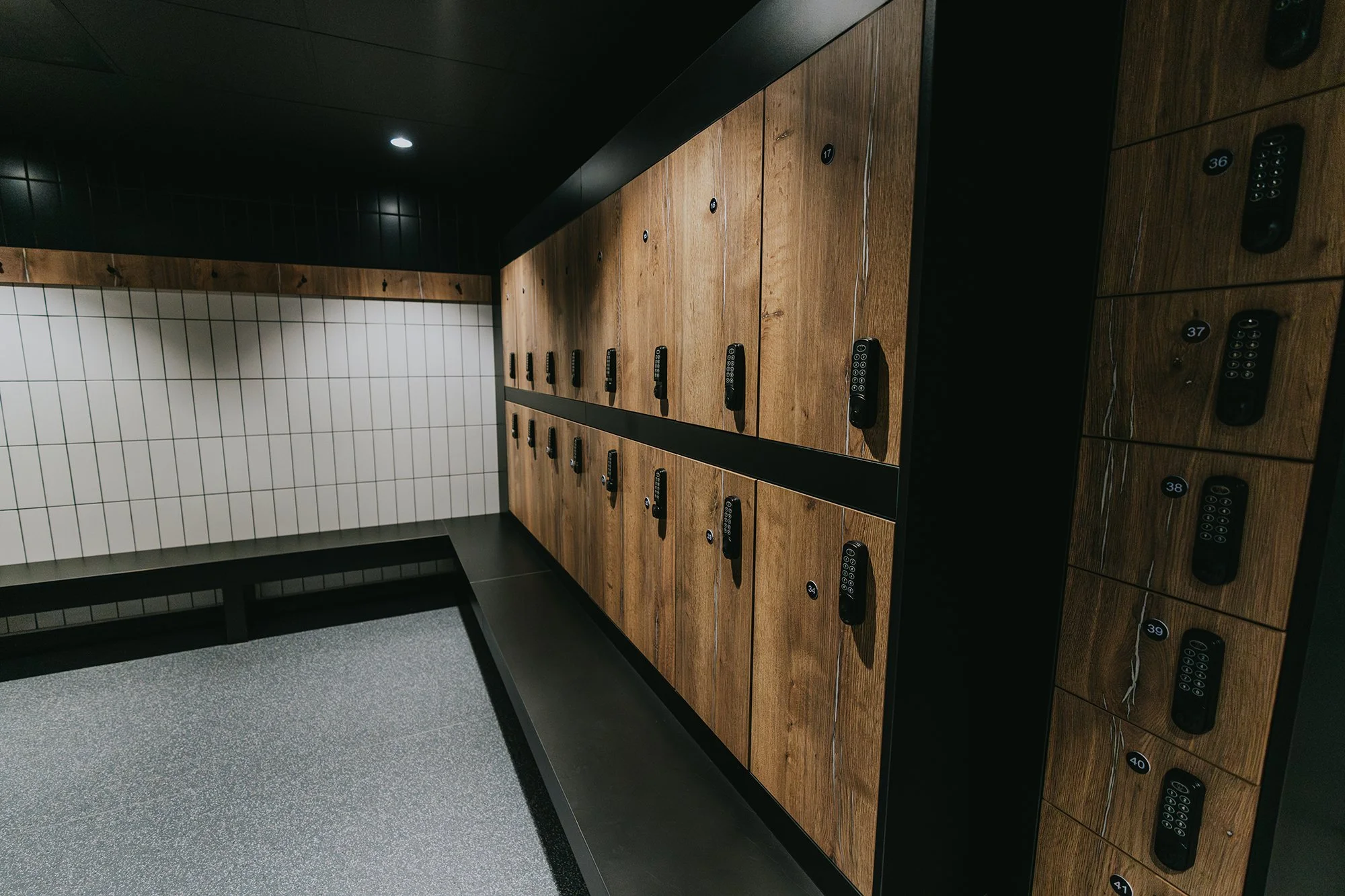 Premium changing facilities, showing lockers with combination locks arranged in a row in a modern space with tiled wall and black ceiling.