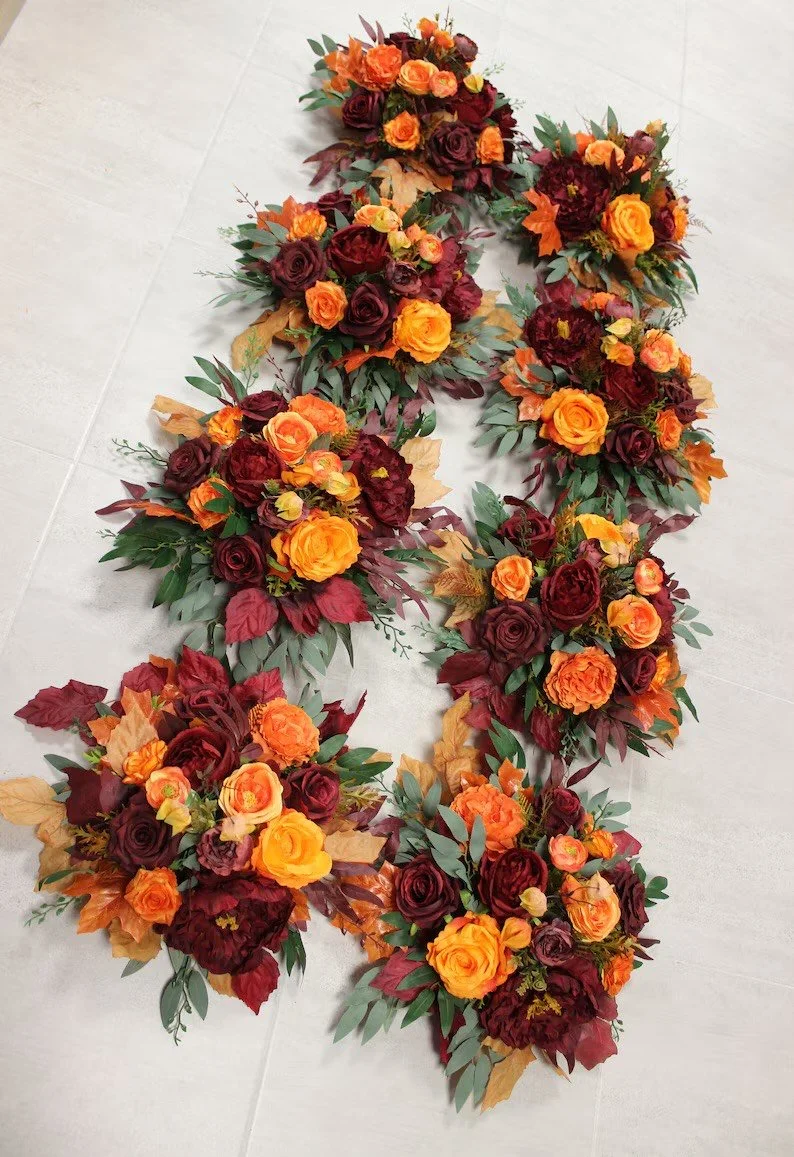 Autumn floral arrangement with roses and leaves in shades of orange, red, and yellow arranged in a U-shape on a light gray tiled floor.