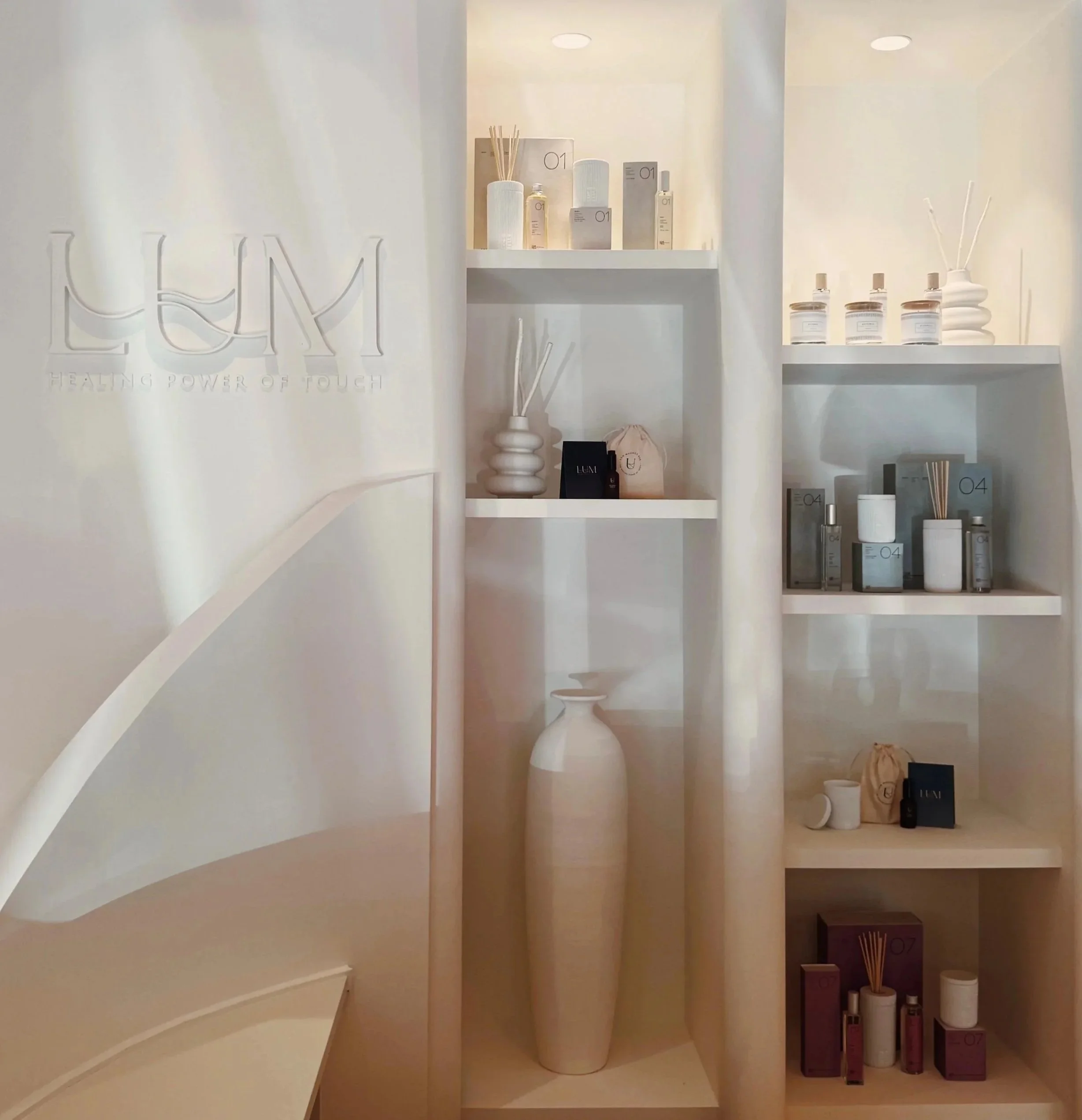 Estantes blancas con productos de spa y aromaterapia, incluido un difusor, perfumes y velas en un ambiente minimalista.