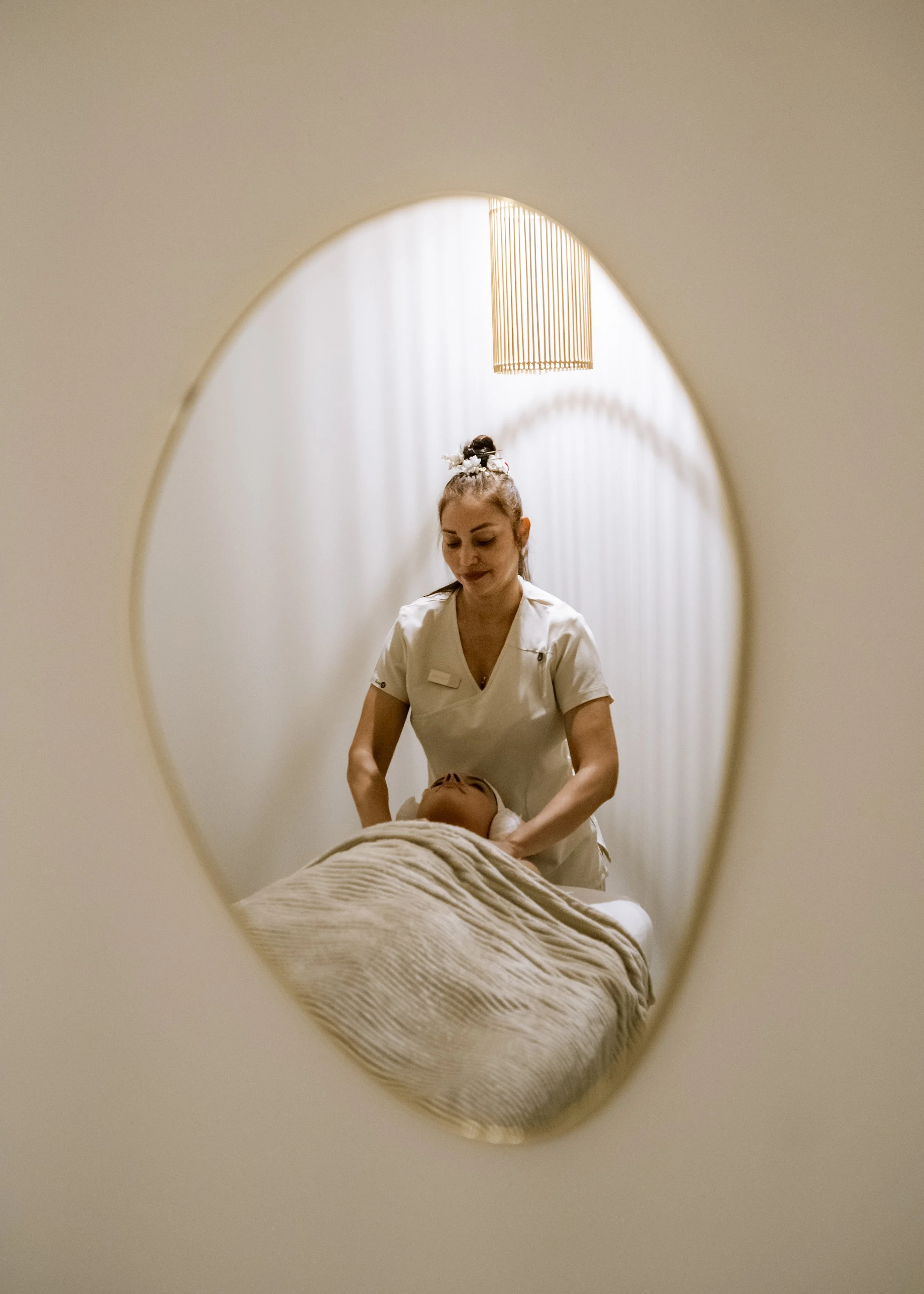 Una terapeuta o masajista atendiendo a una persona en una sala de spa o masaje, visto a través de una ventana redonda.