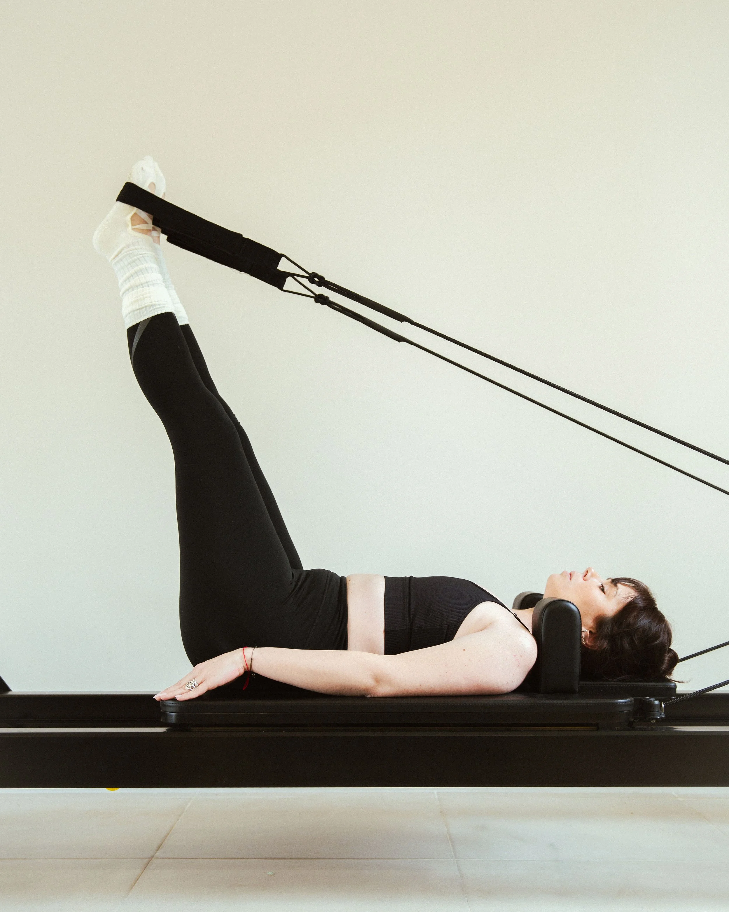 Femme faisant de la rééducation ou de la physiothérapie sur un appareil de Pilates ou de rééducation, allongée sur le dos avec les jambes levées et des bandes de résistance.