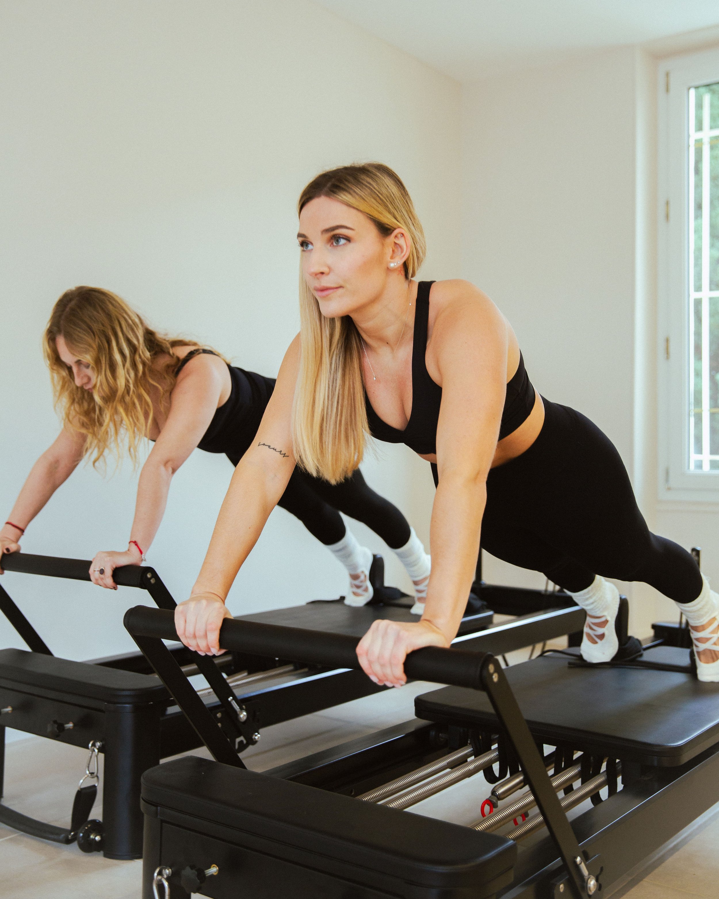 Deux femmes font du Pilates sur des reformers dans une salle bien éclairée.