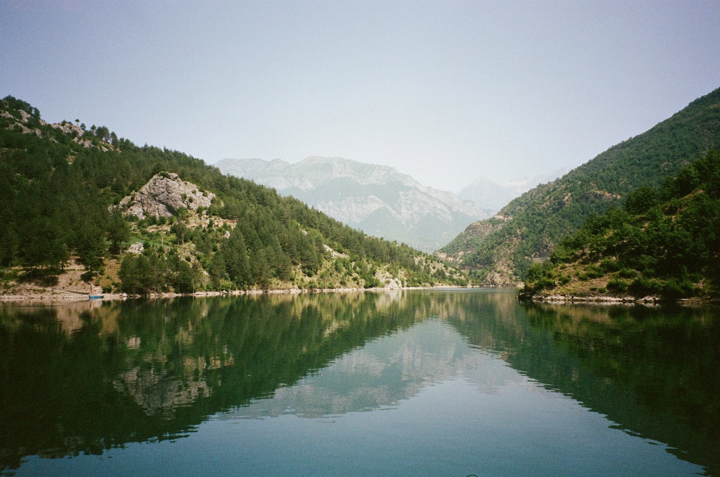 Vue d'un lac entouré de montagnes verdoyantes avec reflet dans l'eau, sous un ciel clair