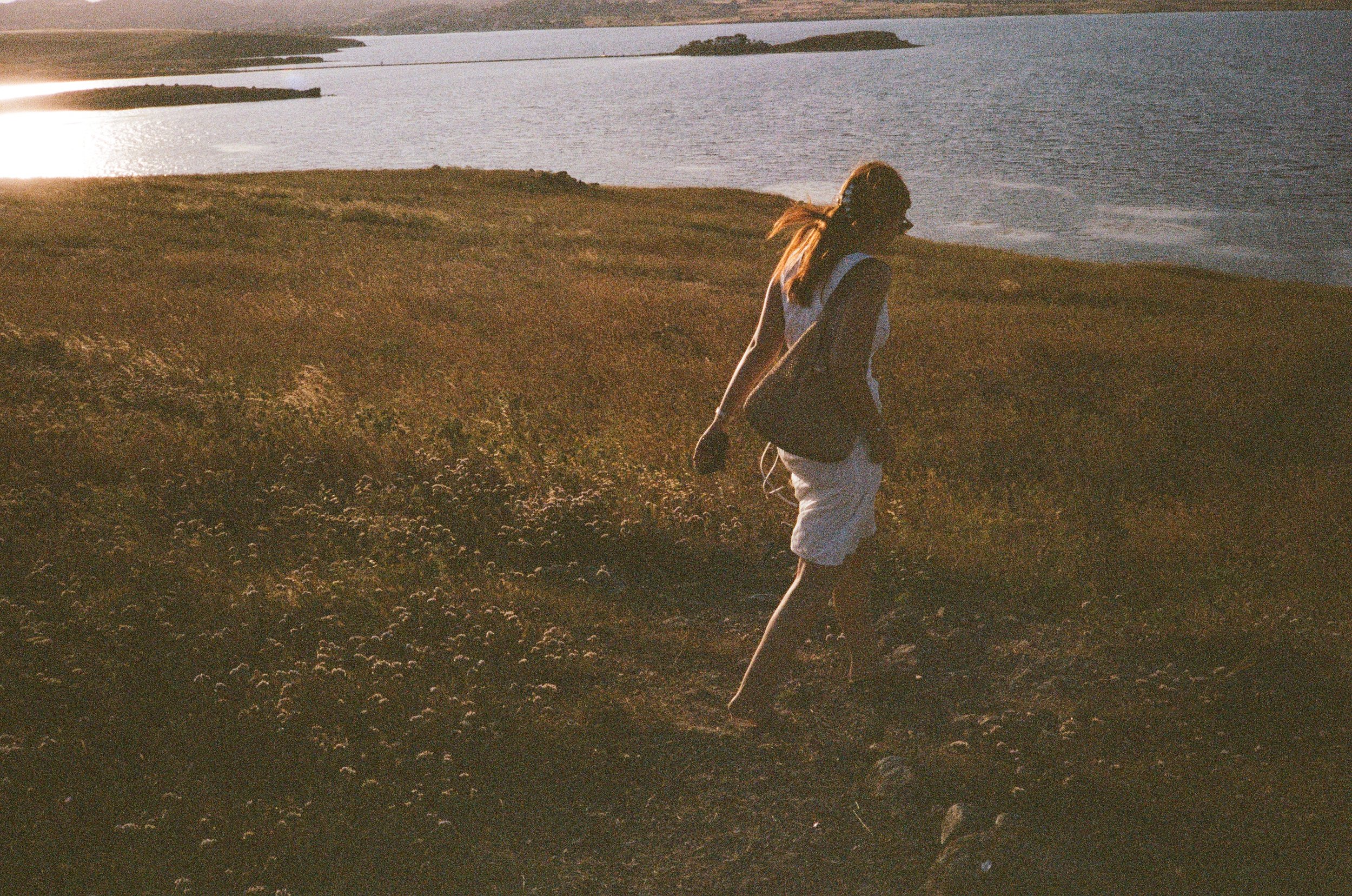 Une personne marchant le long d'une côte au coucher du soleil, portant un sac à dos et des vêtements décontractés.