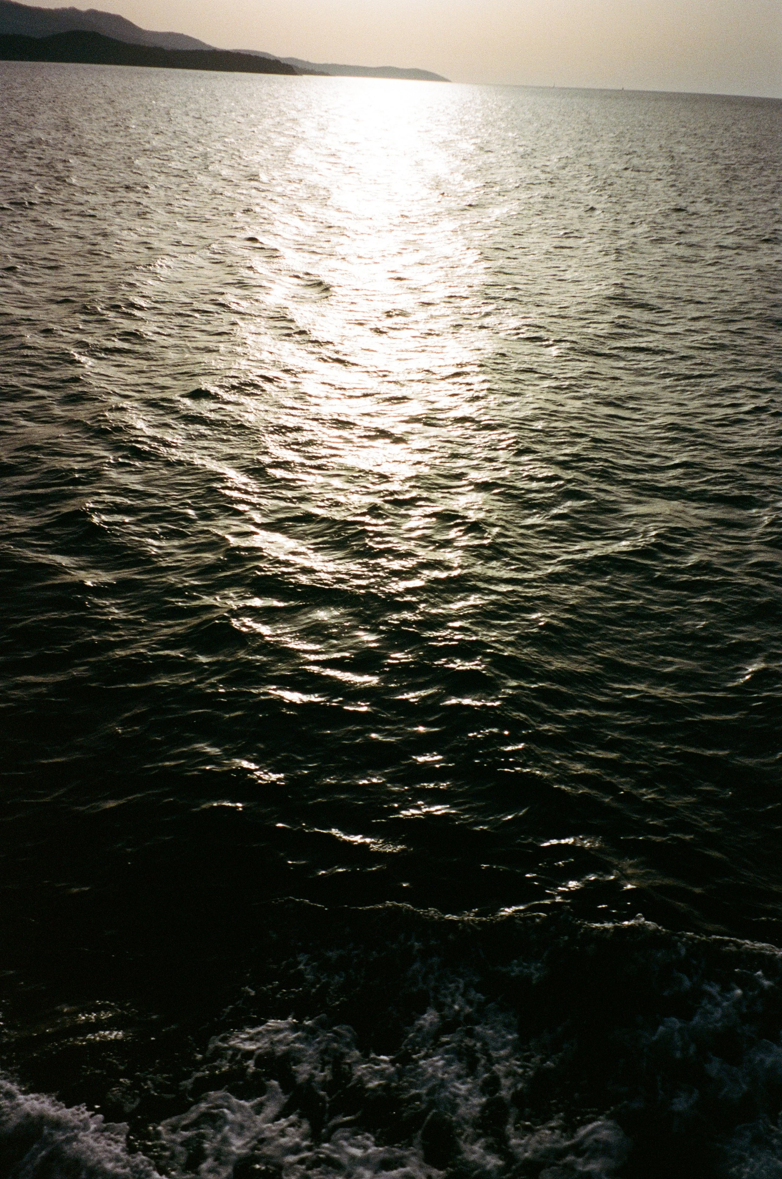 Une mer ou un océan avec des vagues calmes sous un ciel nuageux, avec des montagnes ou des collines au loin, au moment du coucher ou du lever du soleil.