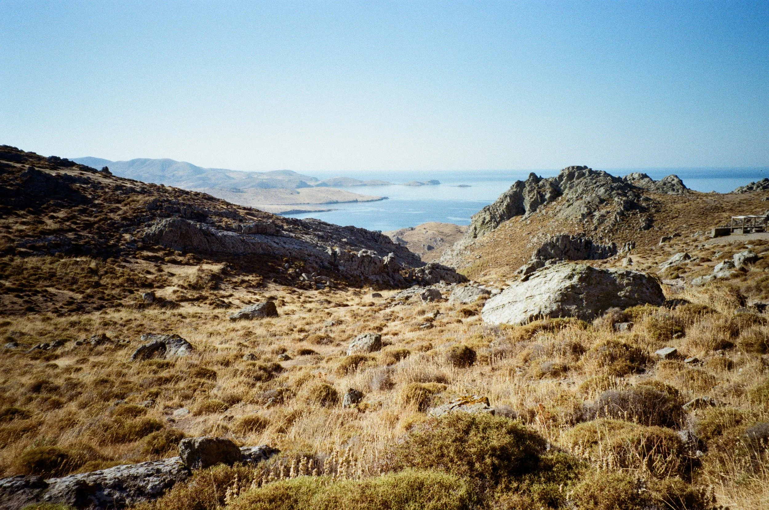 Paysage de montagnes sèches avec des rochers et une vue sur une étendue d'eau, probablement un lac ou une mer, sous un ciel clair.