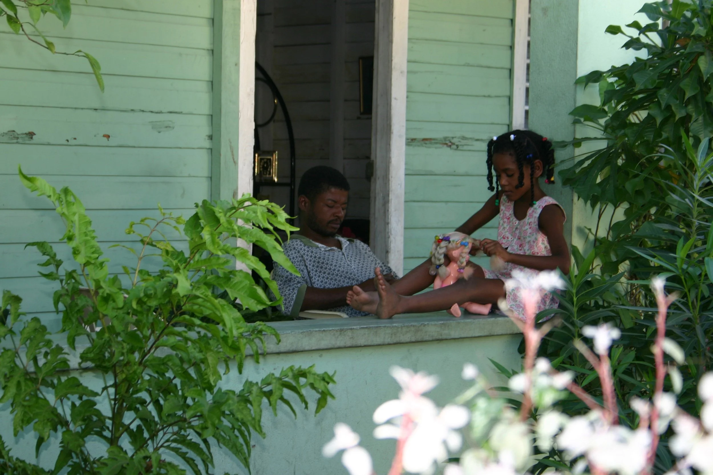 Un homme allongé sur un porche en regardant une jeune fille jouant avec un poupon